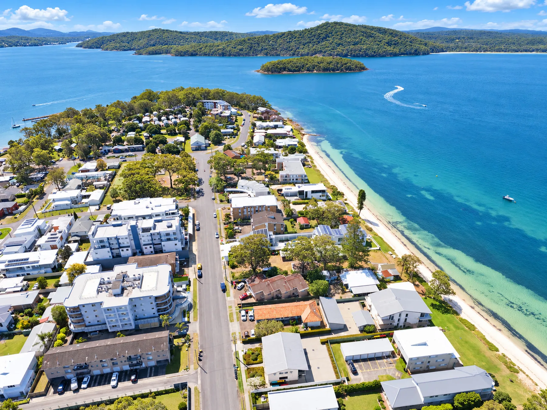 Aerial view of a coastal neighborhood beside a blue bay and green islands.