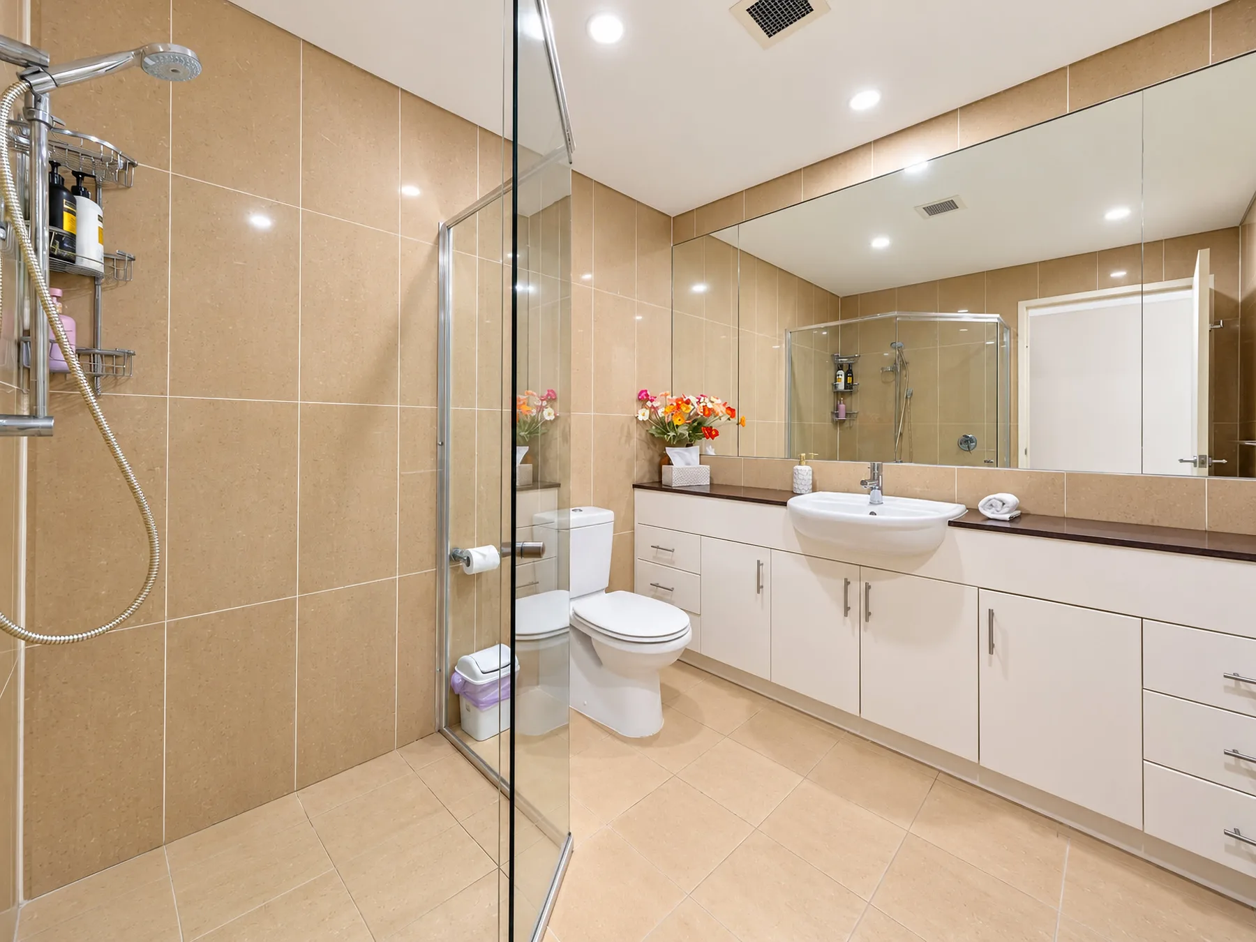 A bathroom with a glass shower, toilet, and long vanity.