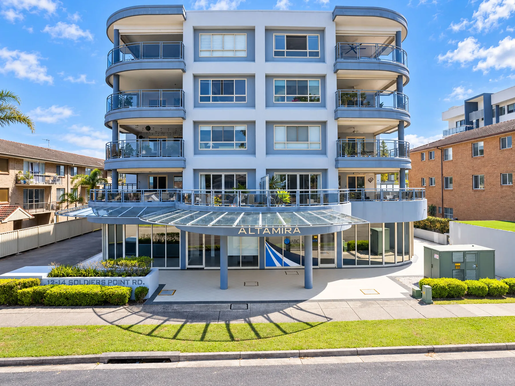 A modern apartment building with curved balconies and a glass entrance canopy.