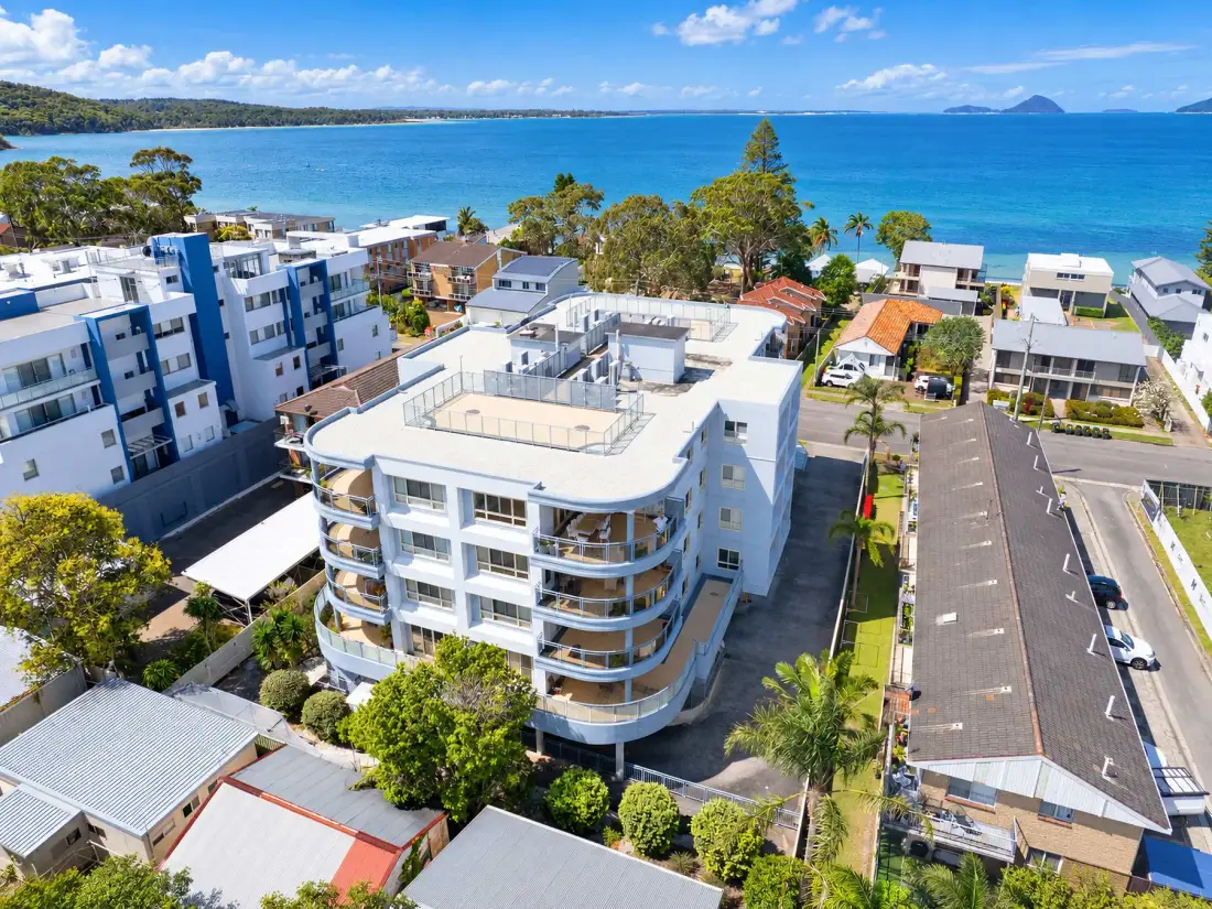 Coastal neighborhood with apartment buildings beside a bright blue bay.