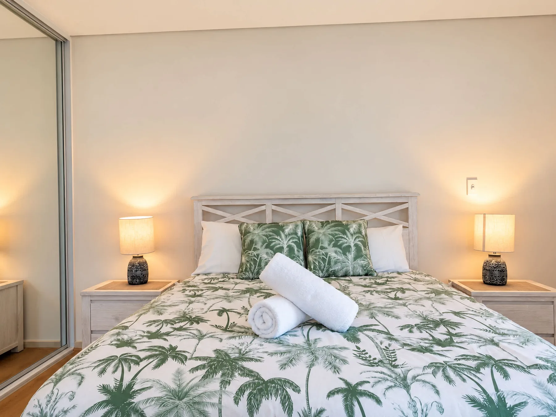 A bedroom with a palm-patterned bedspread and matching bedside lamps.