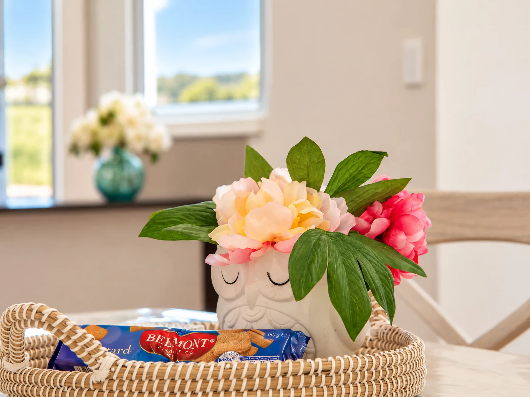 A woven basket with snacks sits beside a flower arrangement on a table.