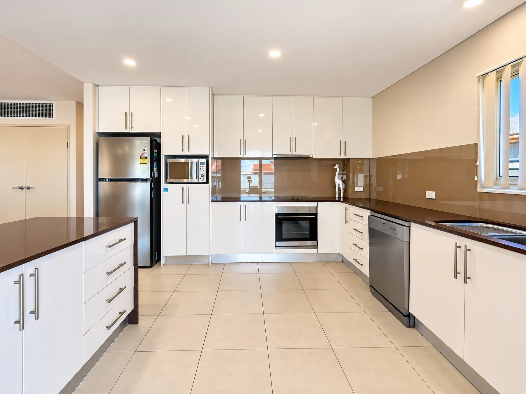 A bright kitchen with white cabinets, tiled flooring, and stainless steel appliances.