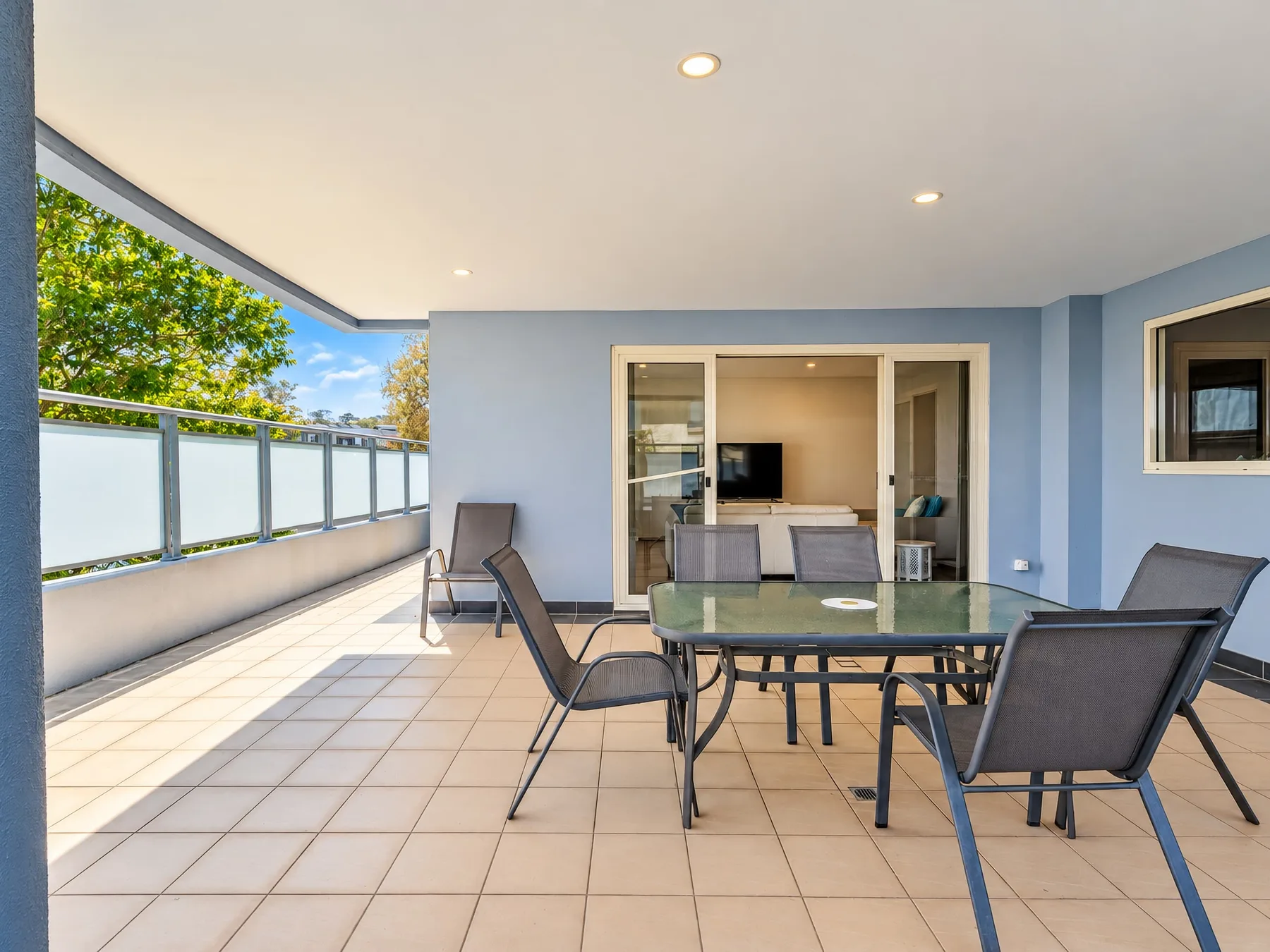 A covered terrace with outdoor seating overlooks leafy trees.