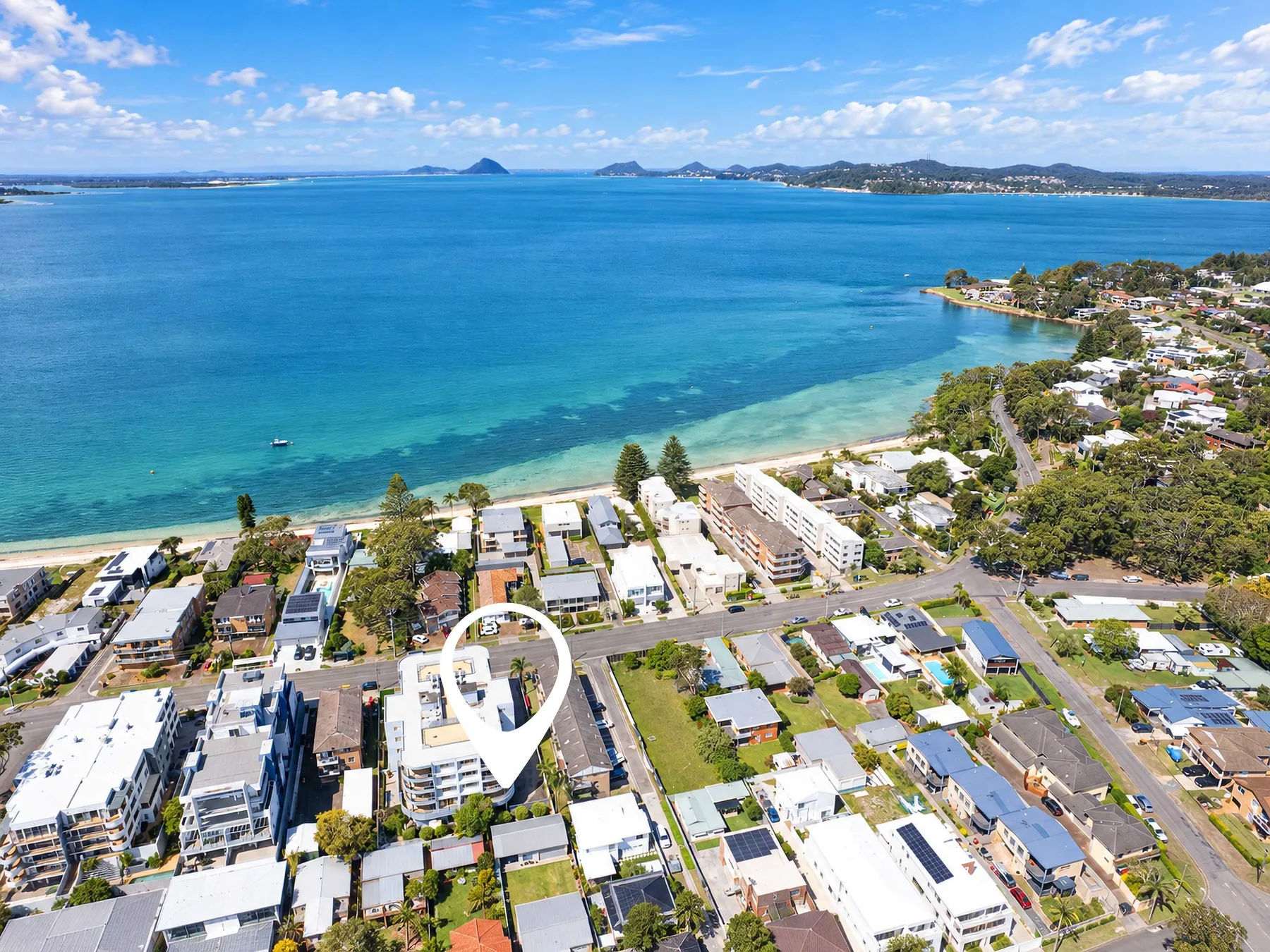 Aerial view of a coastal neighborhood beside a broad blue bay.