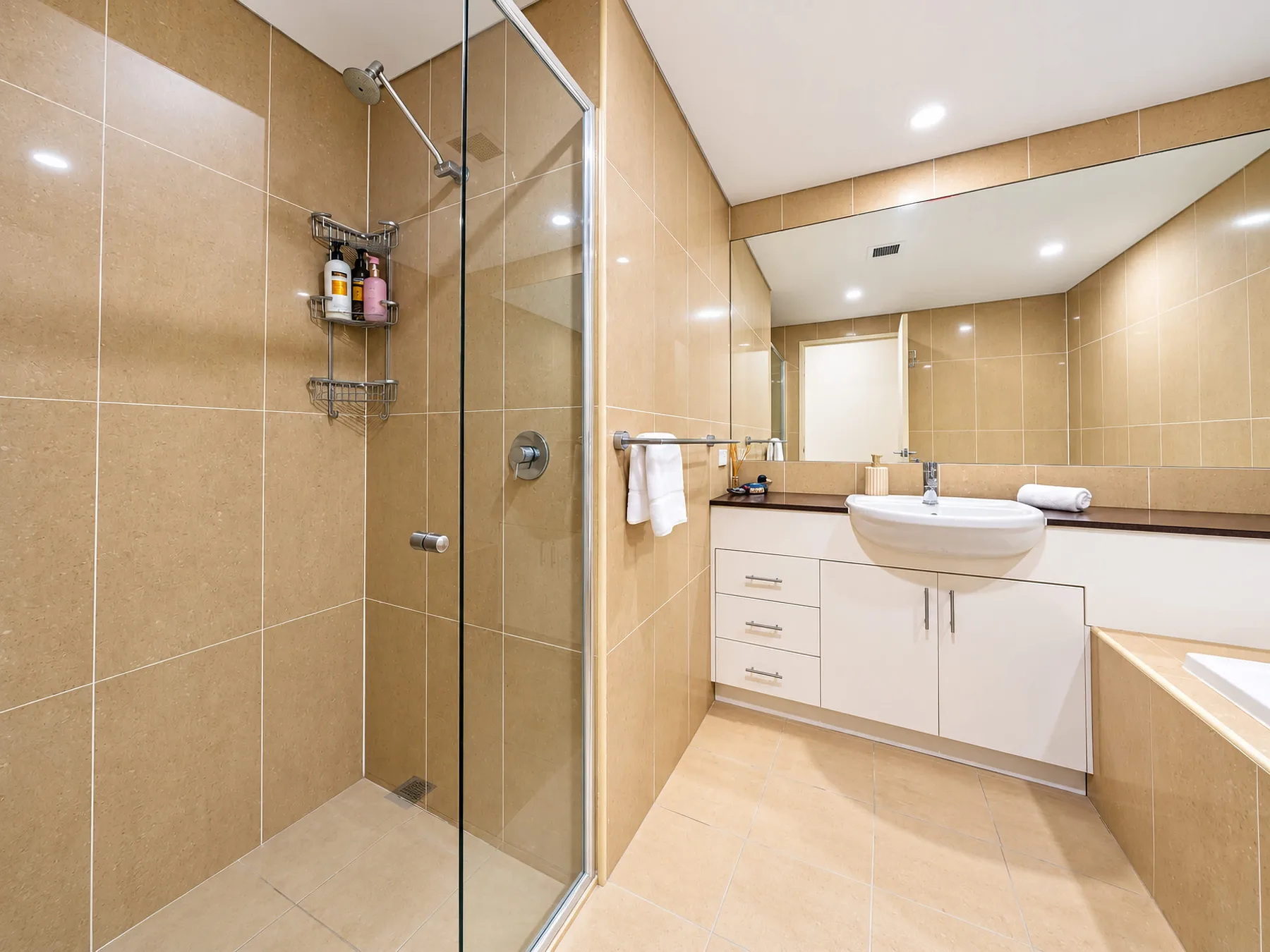 A tiled bathroom with a glass shower and a sink vanity.