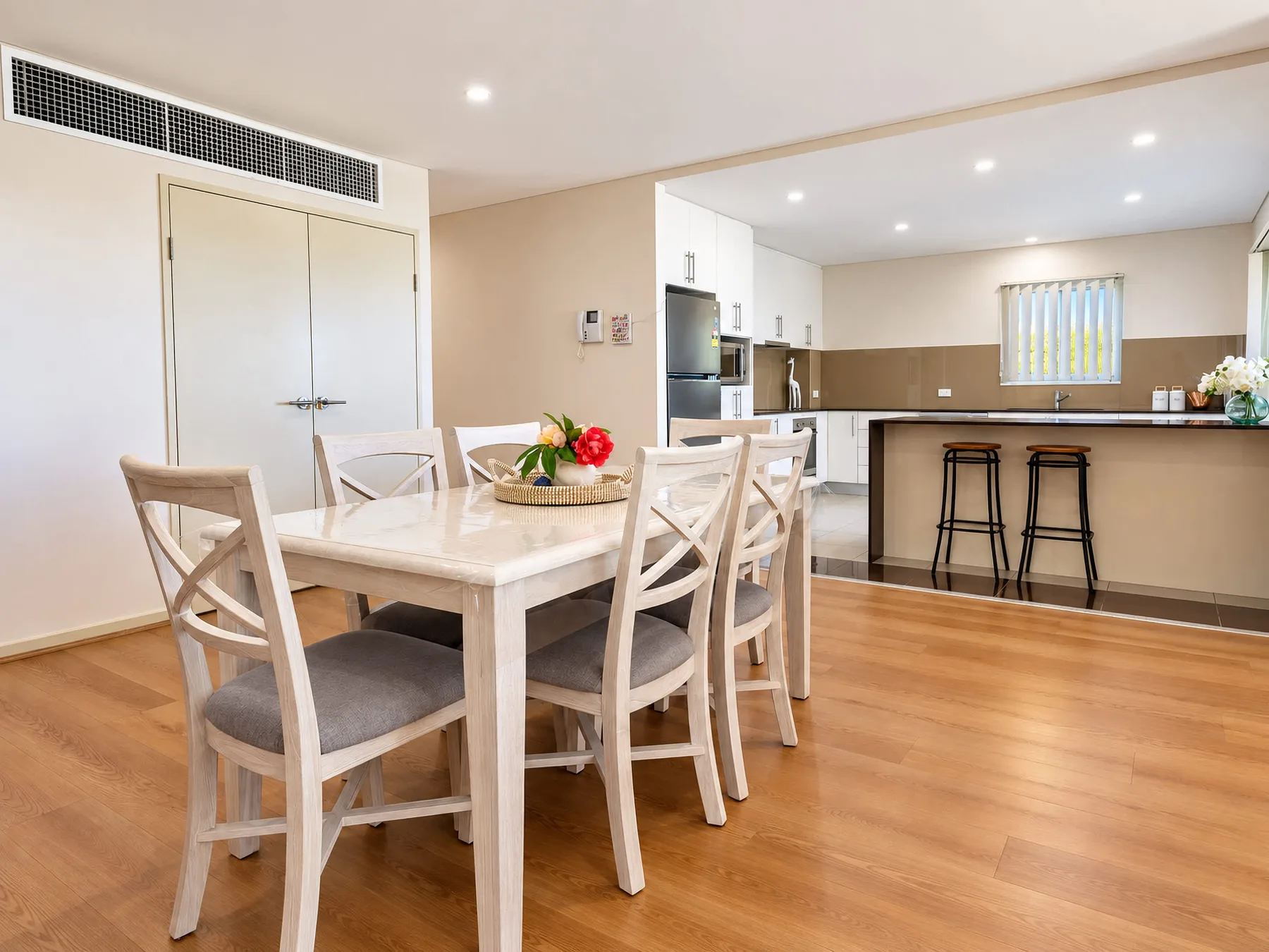 An open-plan dining area and kitchen with a wooden table and breakfast bar.