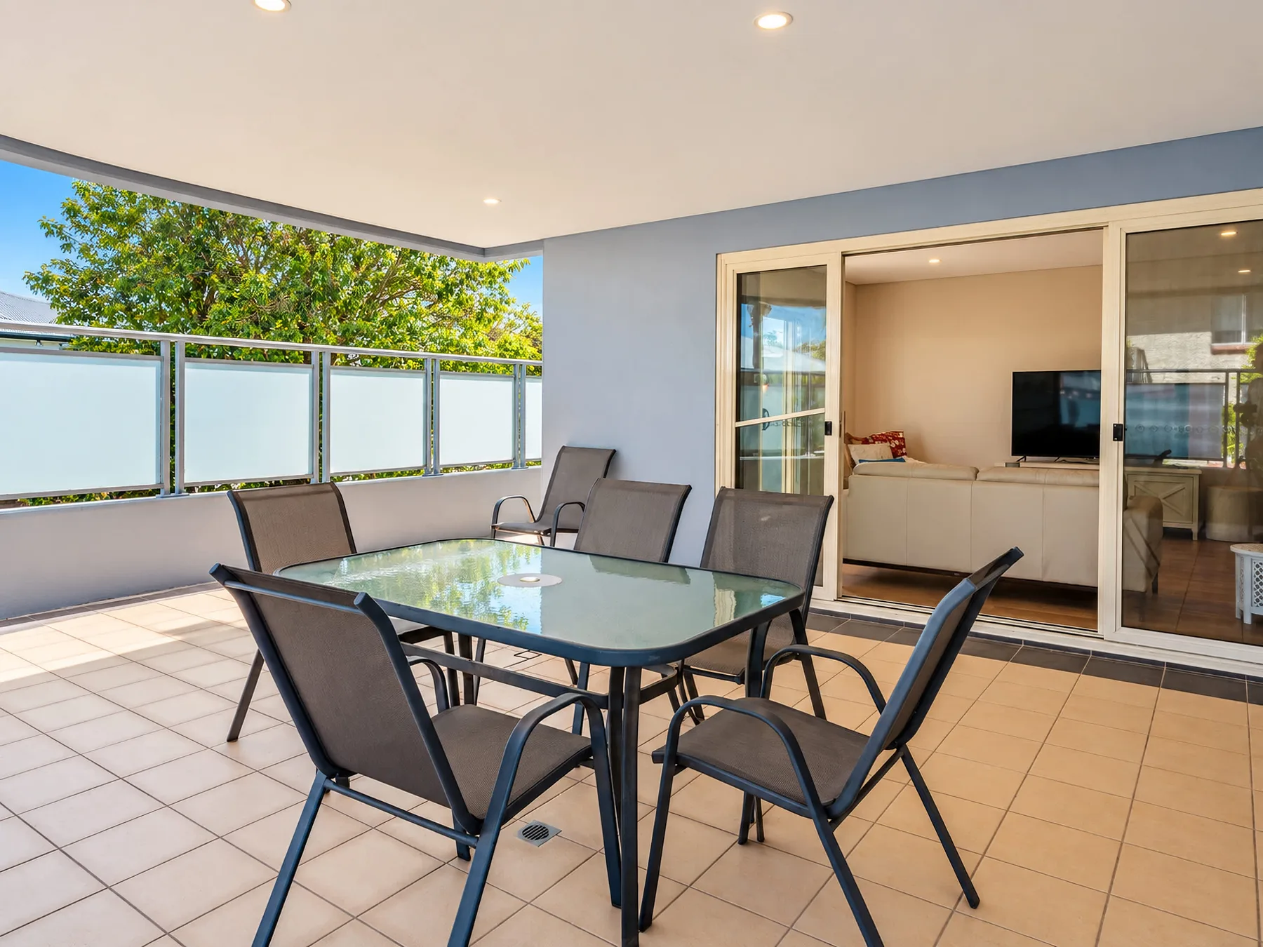 A tiled patio has a glass dining table and seating beside sliding doors.