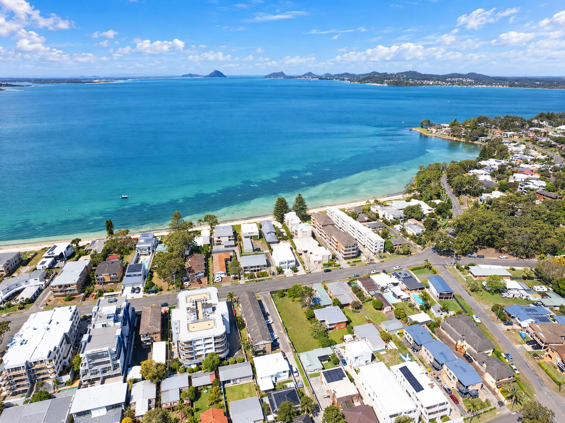Aerial coastal view of a seaside neighborhood beside a broad blue bay.