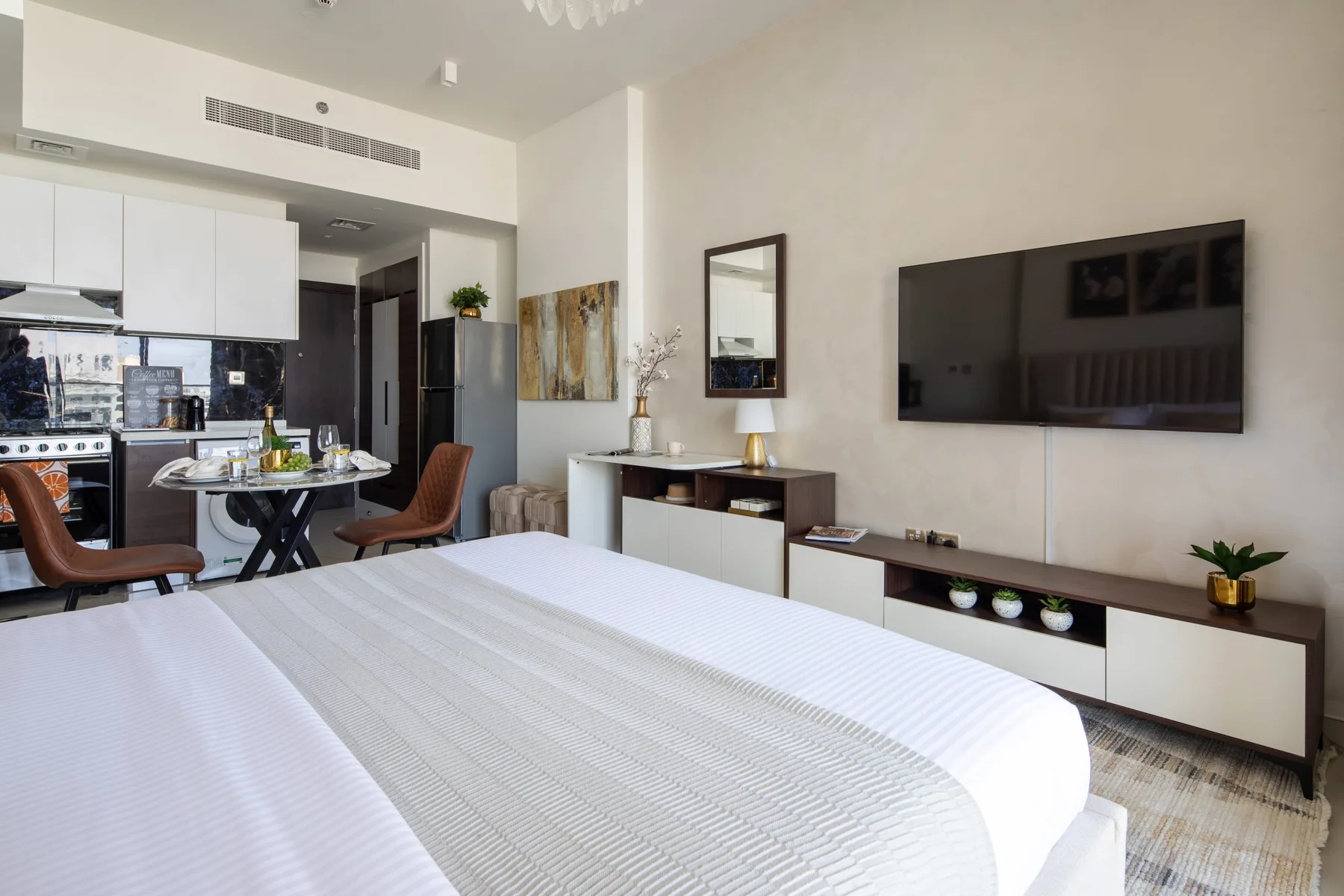 A bedroom with a large bed, a wall-mounted television, and an adjoining dining area.