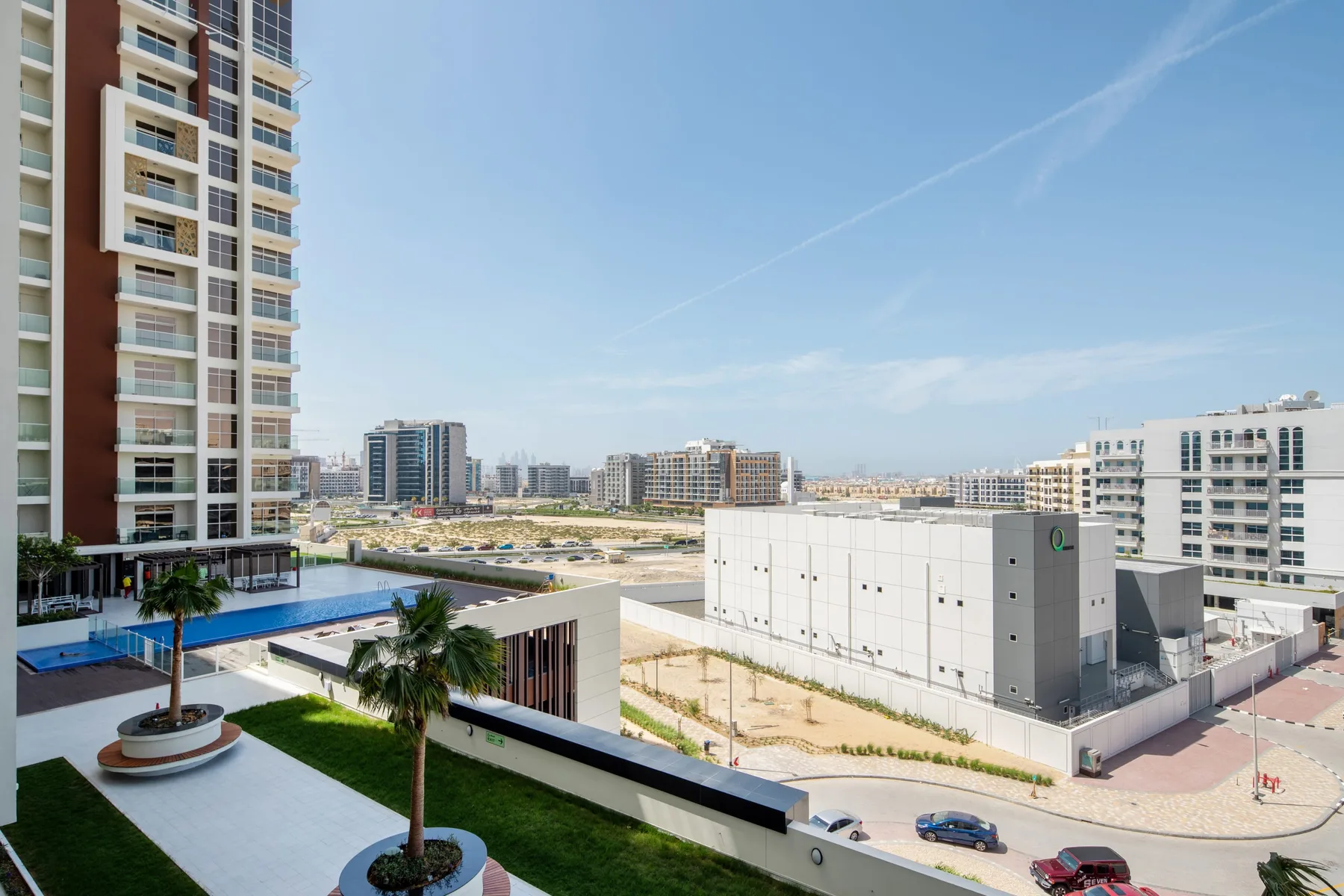 A cityscape with modern apartment buildings, a pool, and landscaped grounds under a clear sky.