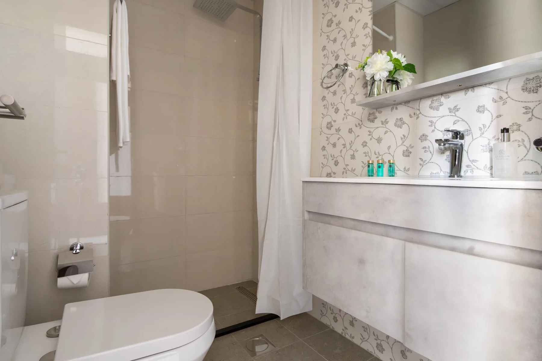 A bathroom with a shower curtain, toilet, and sink beneath floral-patterned walls.