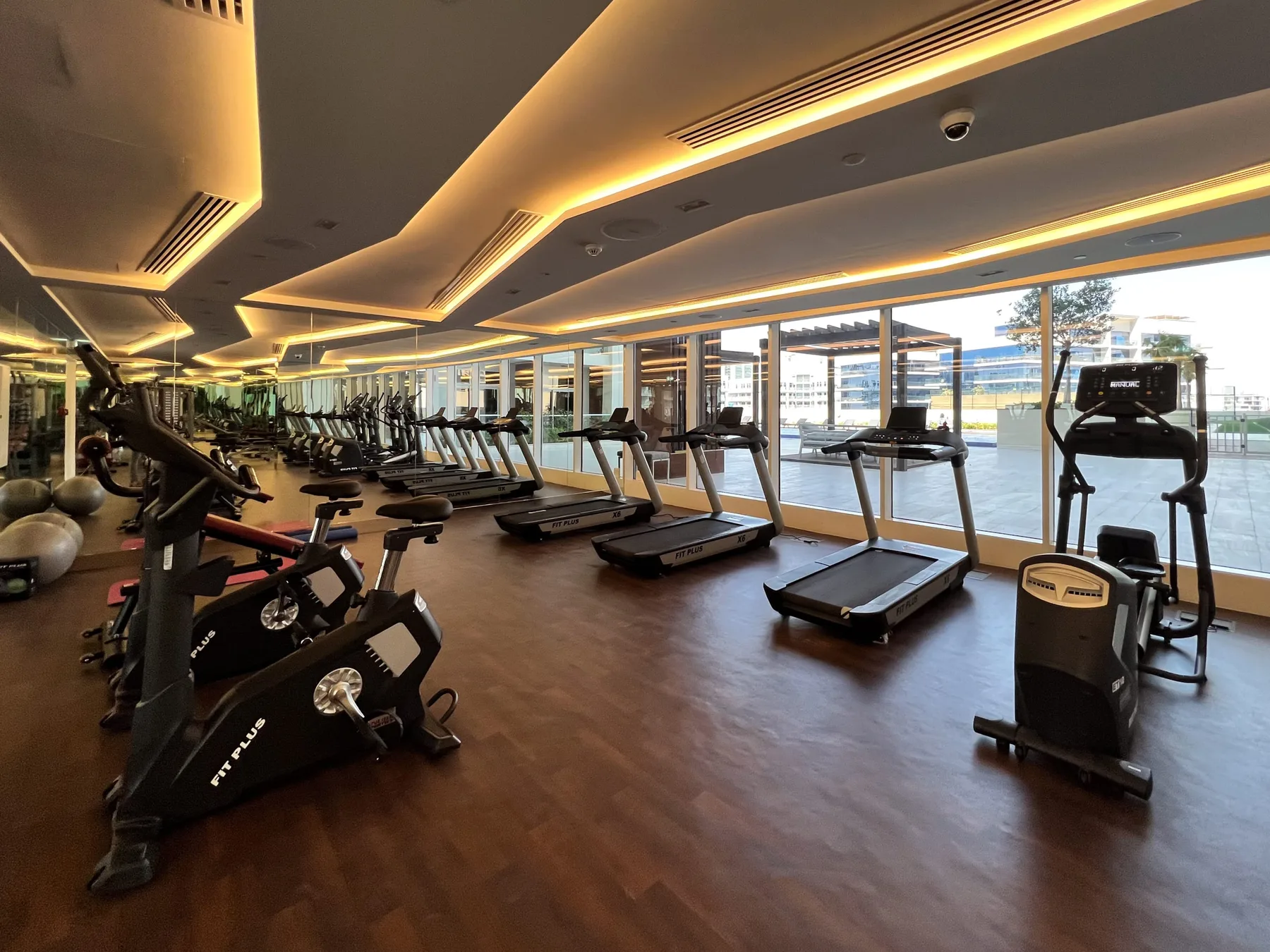 A gym with rows of exercise equipment beside large windows.