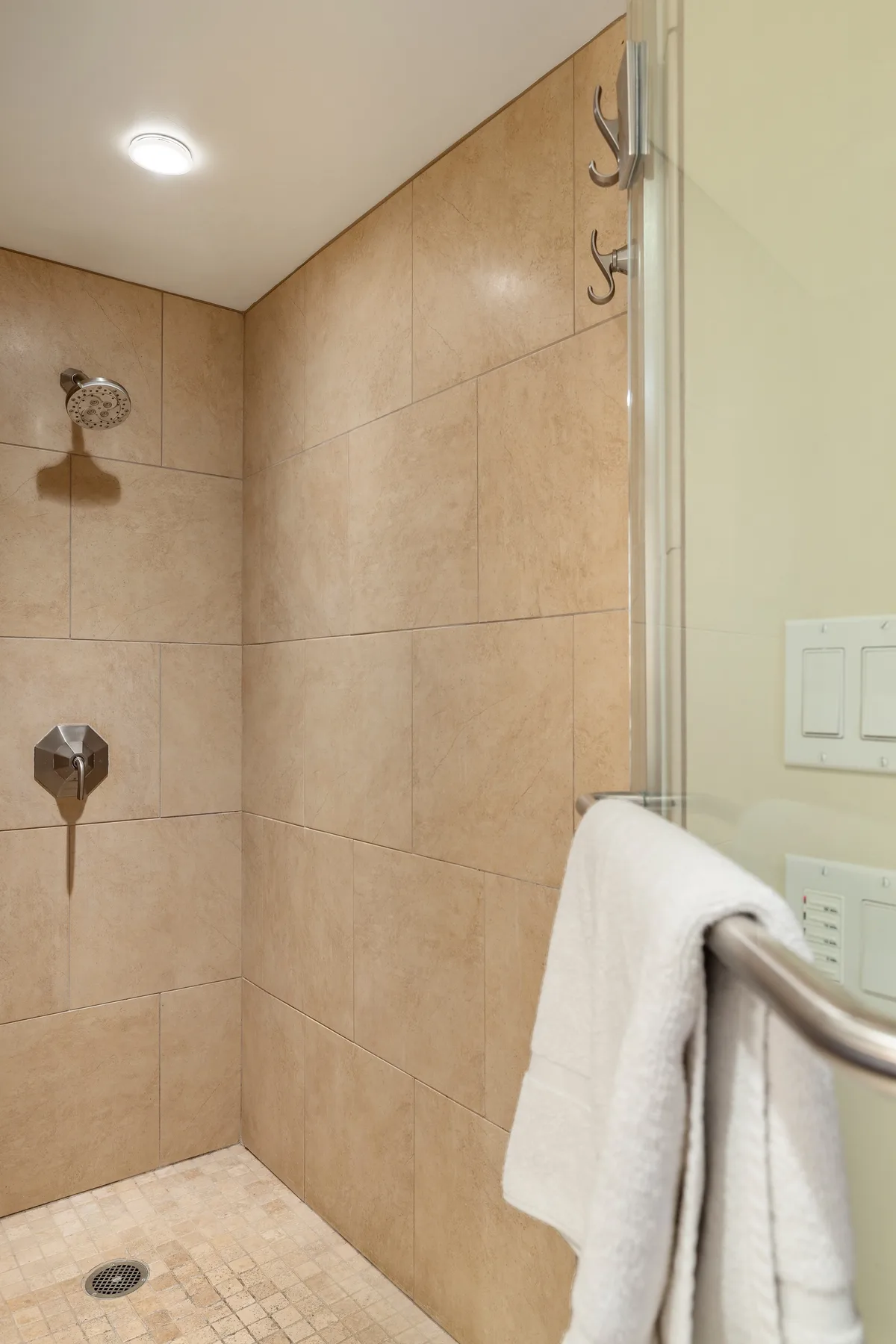 Una ducha con azulejos, cabezal, controles y una toalla colgada cerca.