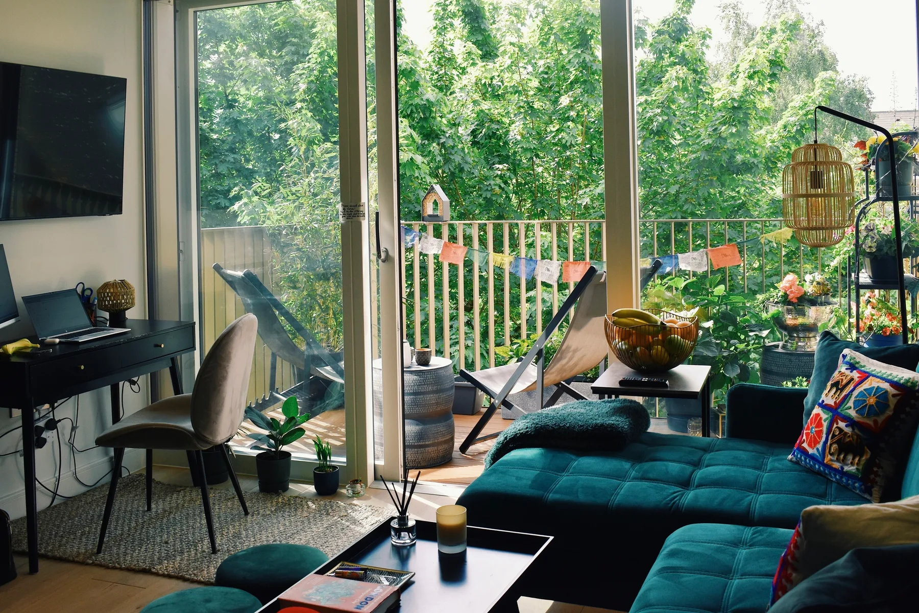 A living room opens onto a balcony with seating and leafy views.
