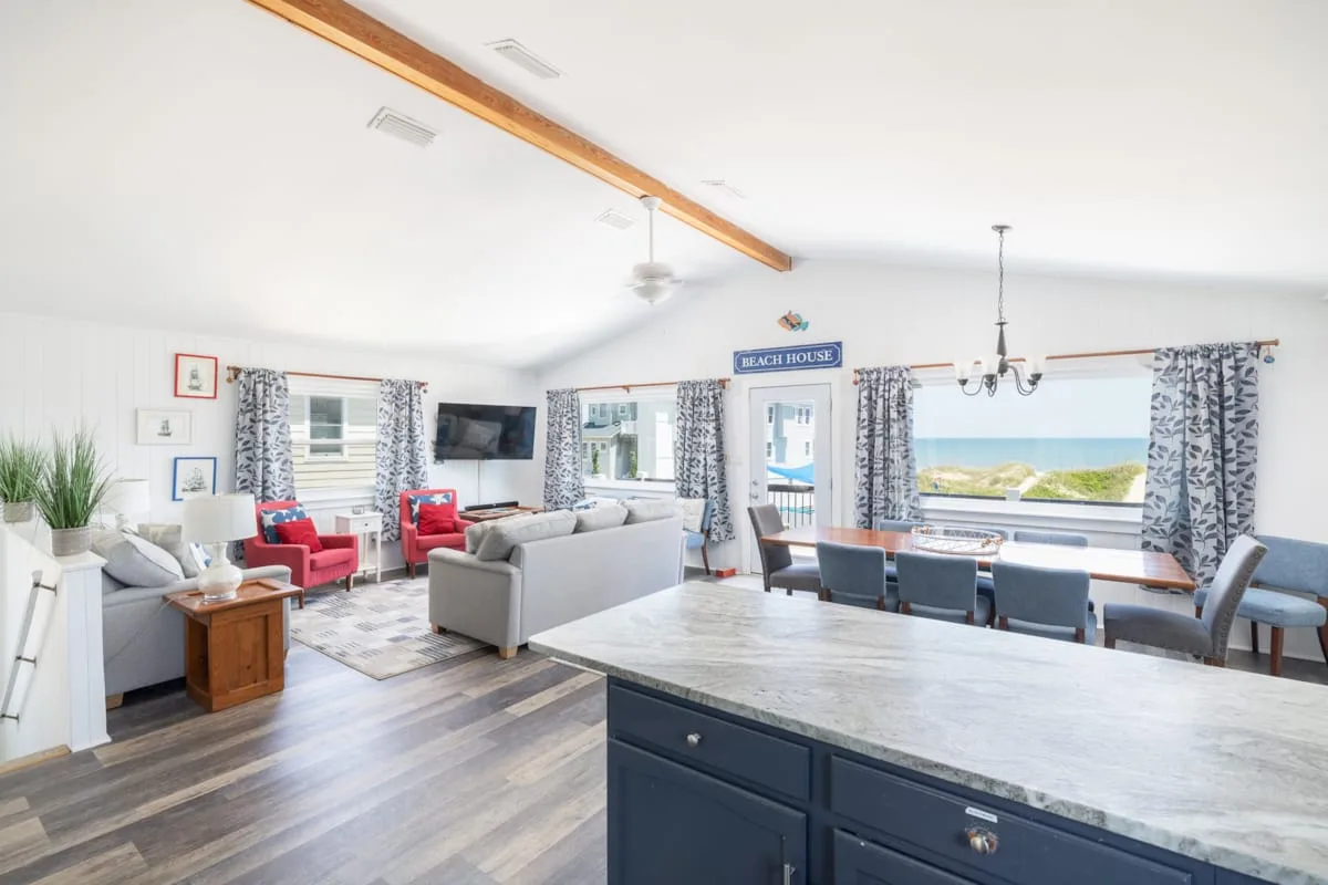 An open living and dining area has seating beside large windows overlooking the water.