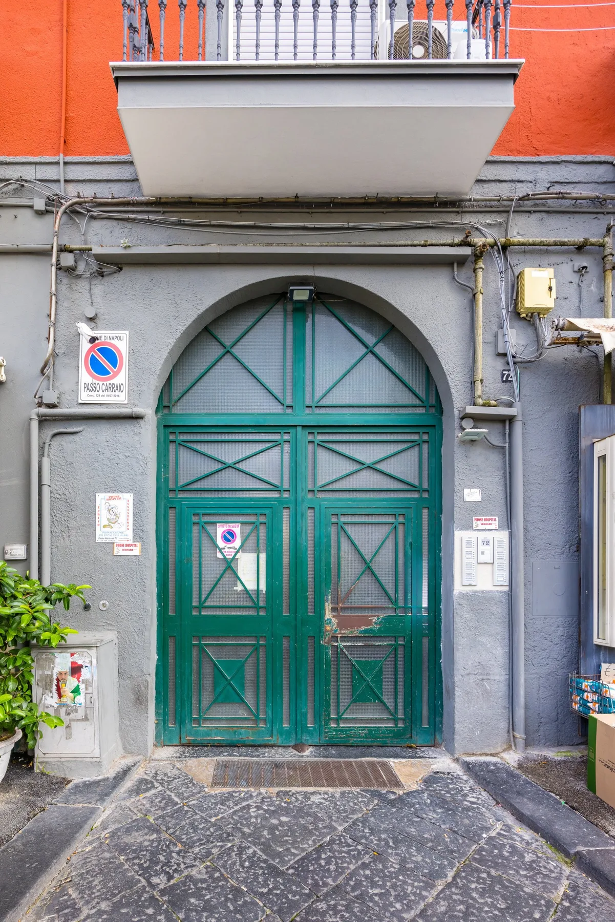 Una entrada verde arqueada en una fachada gris, bajo un muro superior naranja.