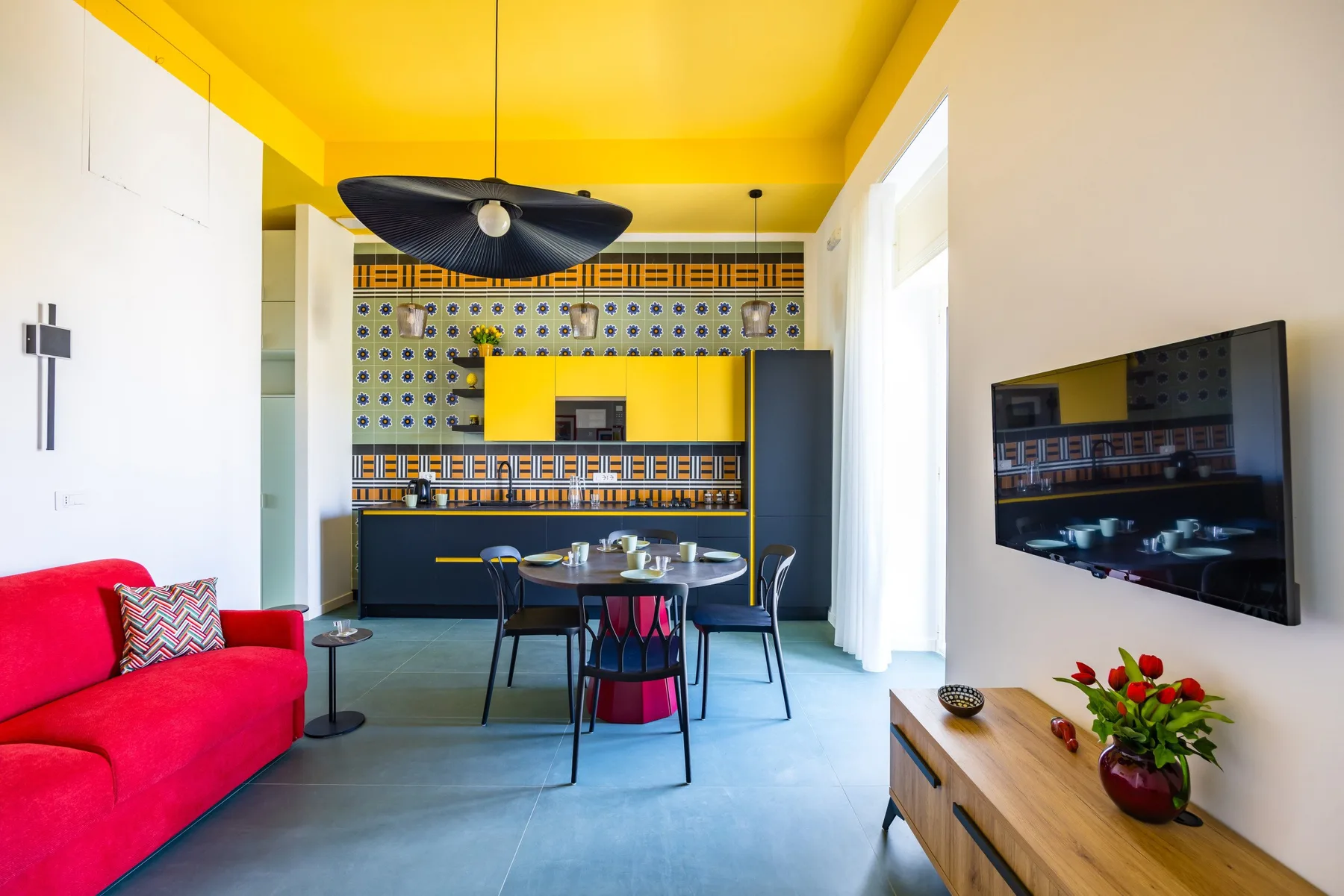 Una colorida sala con comedor cuenta con un sofá rojo y una cocina abierta.