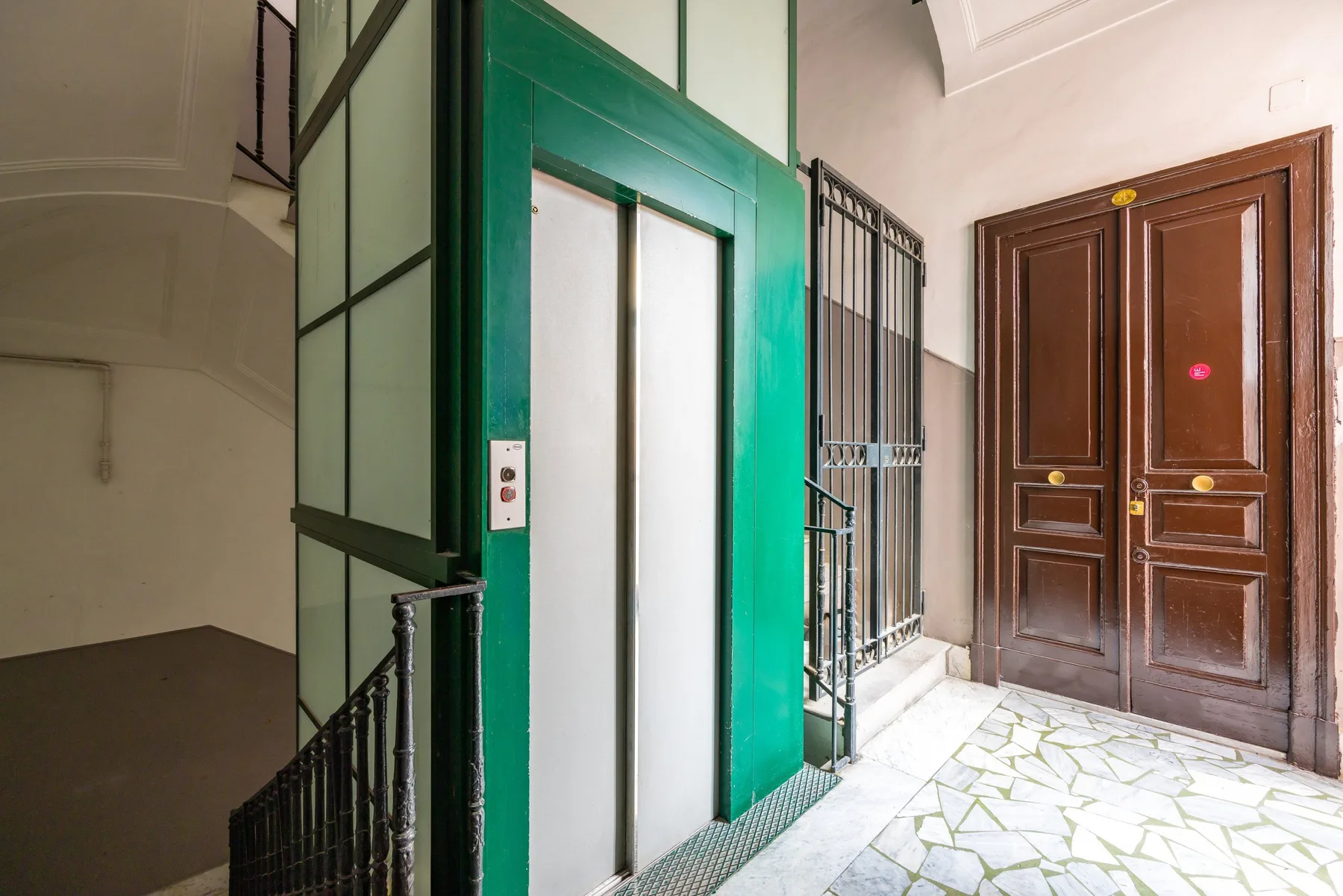 Un pasillo de edificio con un ascensor verde y puertas de madera oscura.