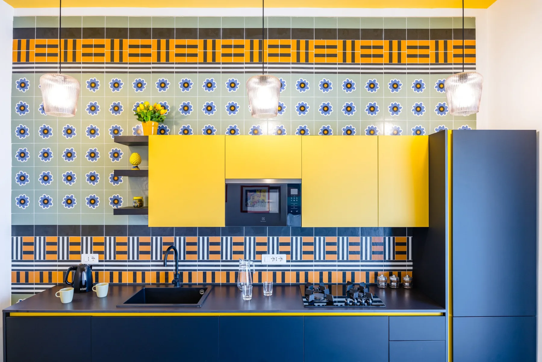 Una cocina luminosa con gabinetes amarillos, azulejos estampados y una encimera oscura.