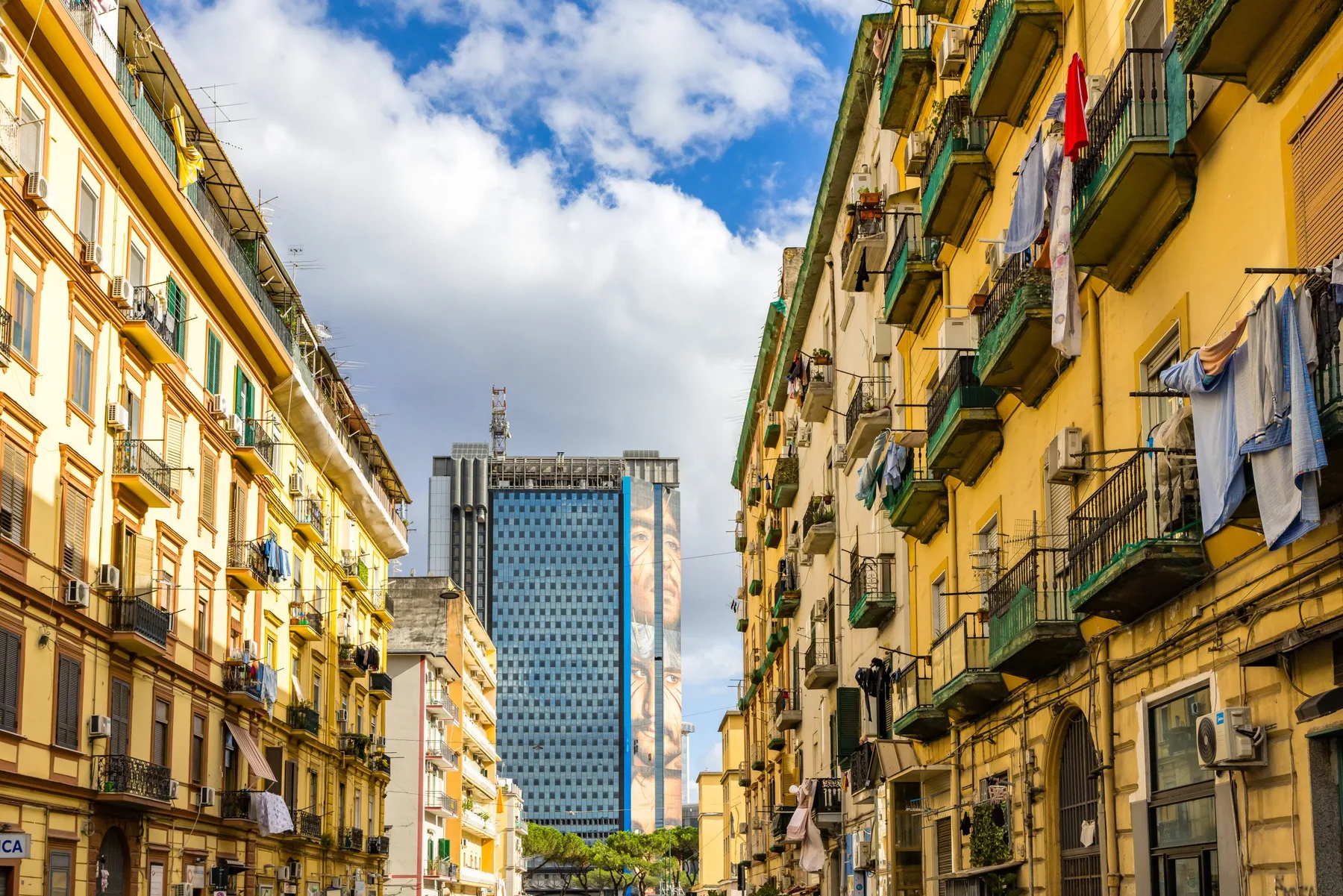 Una calle urbana flanqueada por edificios residenciales, con un edificio moderno más alto a lo lejos.
