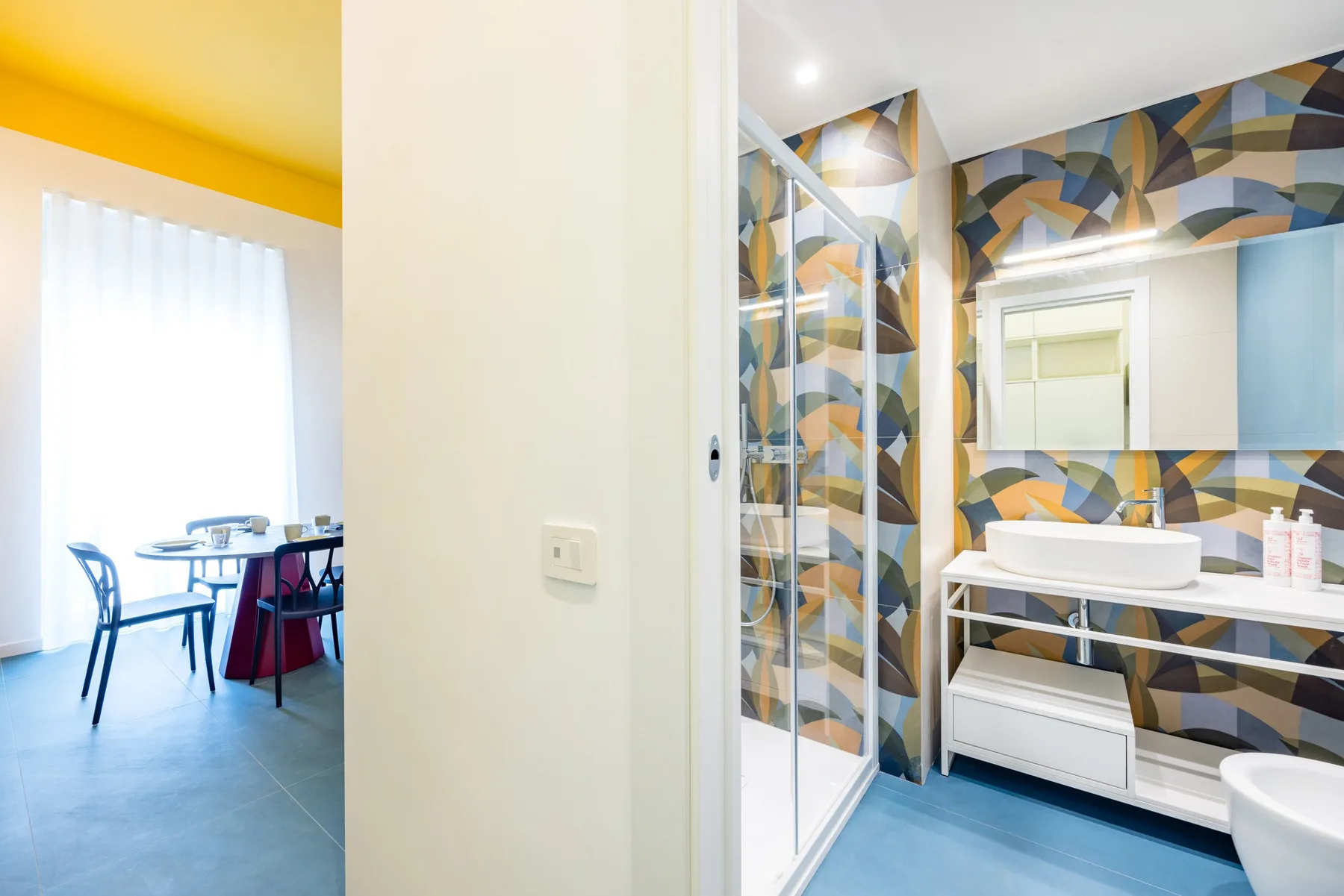 Un baño con ducha de vidrio y tocador, junto a un comedor.