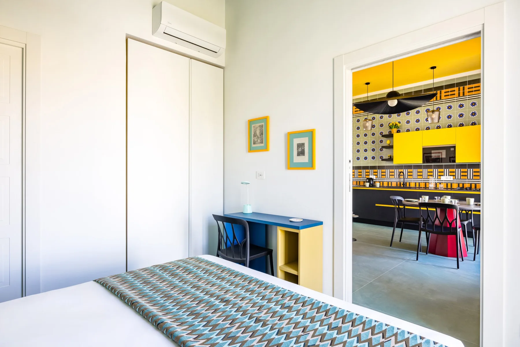 Un dormitorio luminoso con una colcha estampada y un escritorio junto a la puerta.