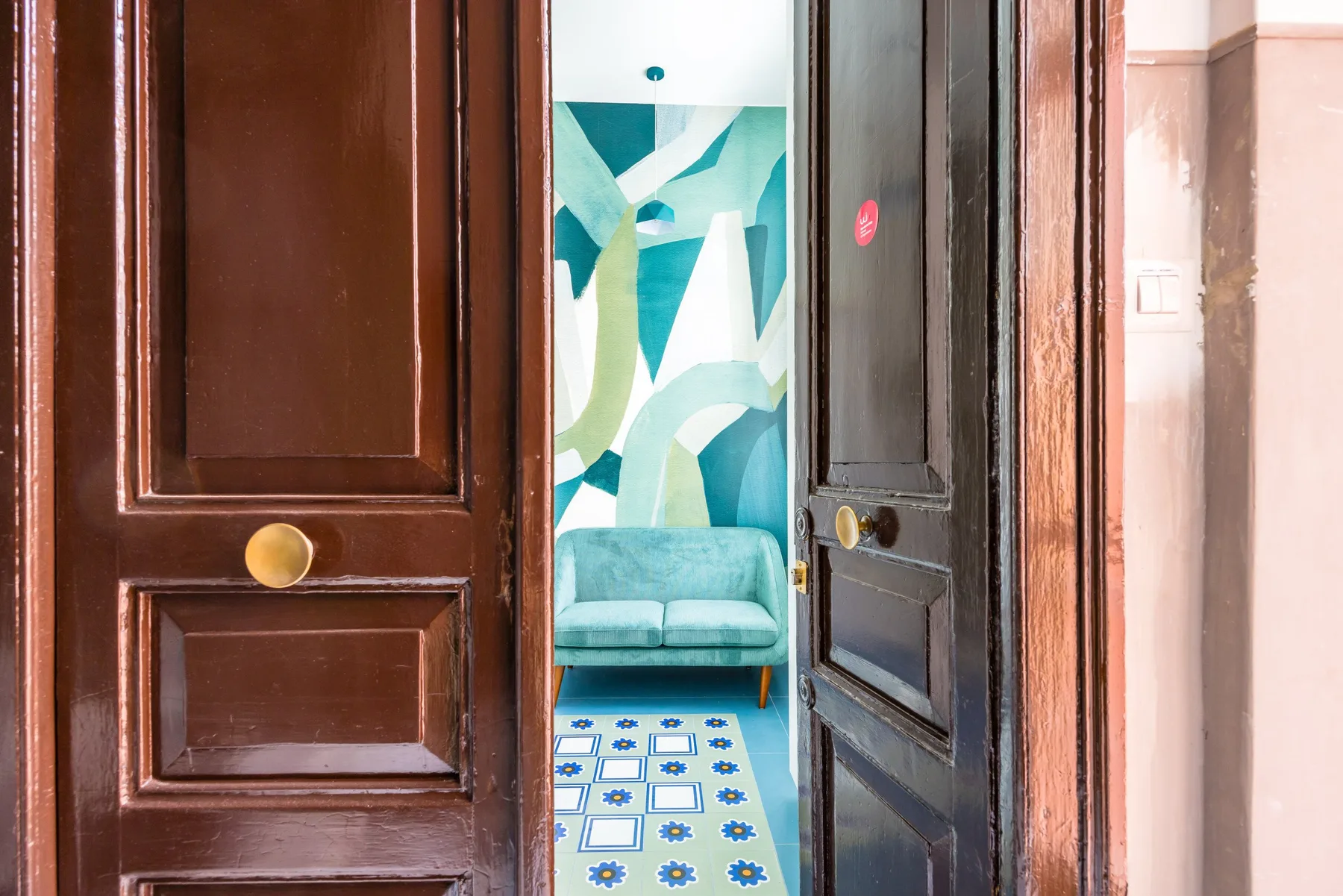 Una puerta da a una habitación con asientos color turquesa y una alfombra azul estampada.