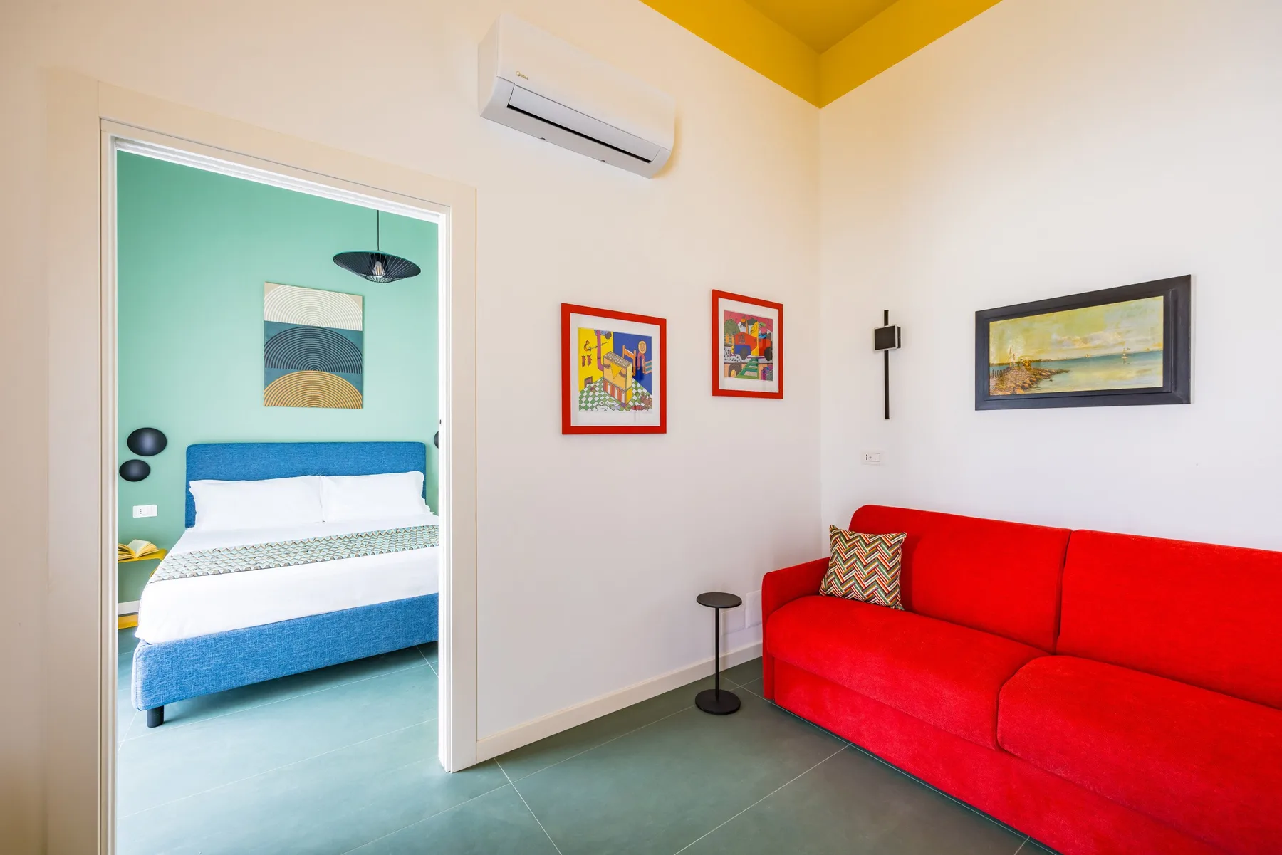 Una luminosa sala de estar con asientos rojos y una puerta abierta a un dormitorio.