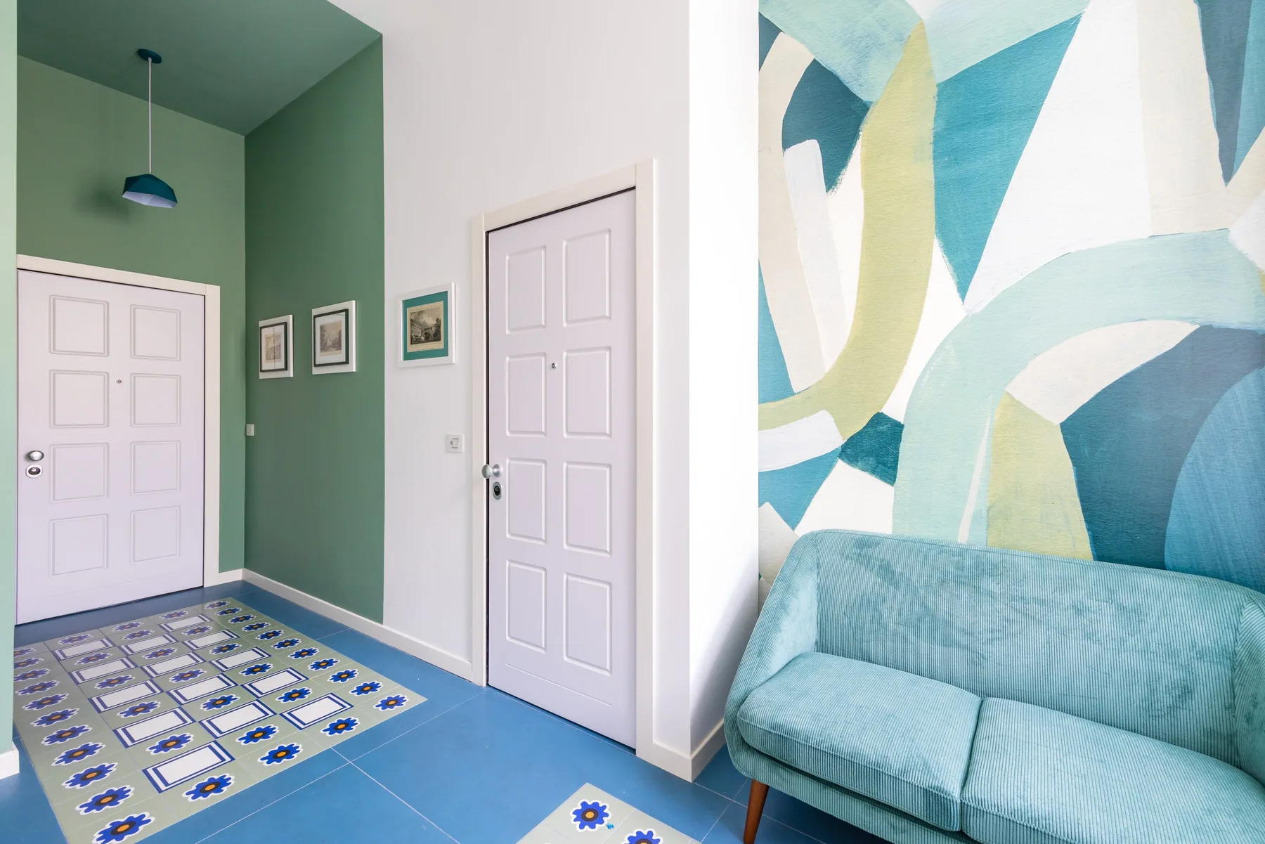 Una entrada colorida con puertas blancas, suelo estampado y un sofá verde azulado.