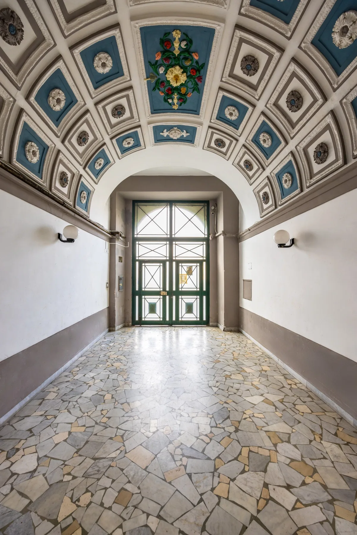 Un pasillo decorado conduce a una puerta alta de vidrio bajo una bóveda ornamentada.