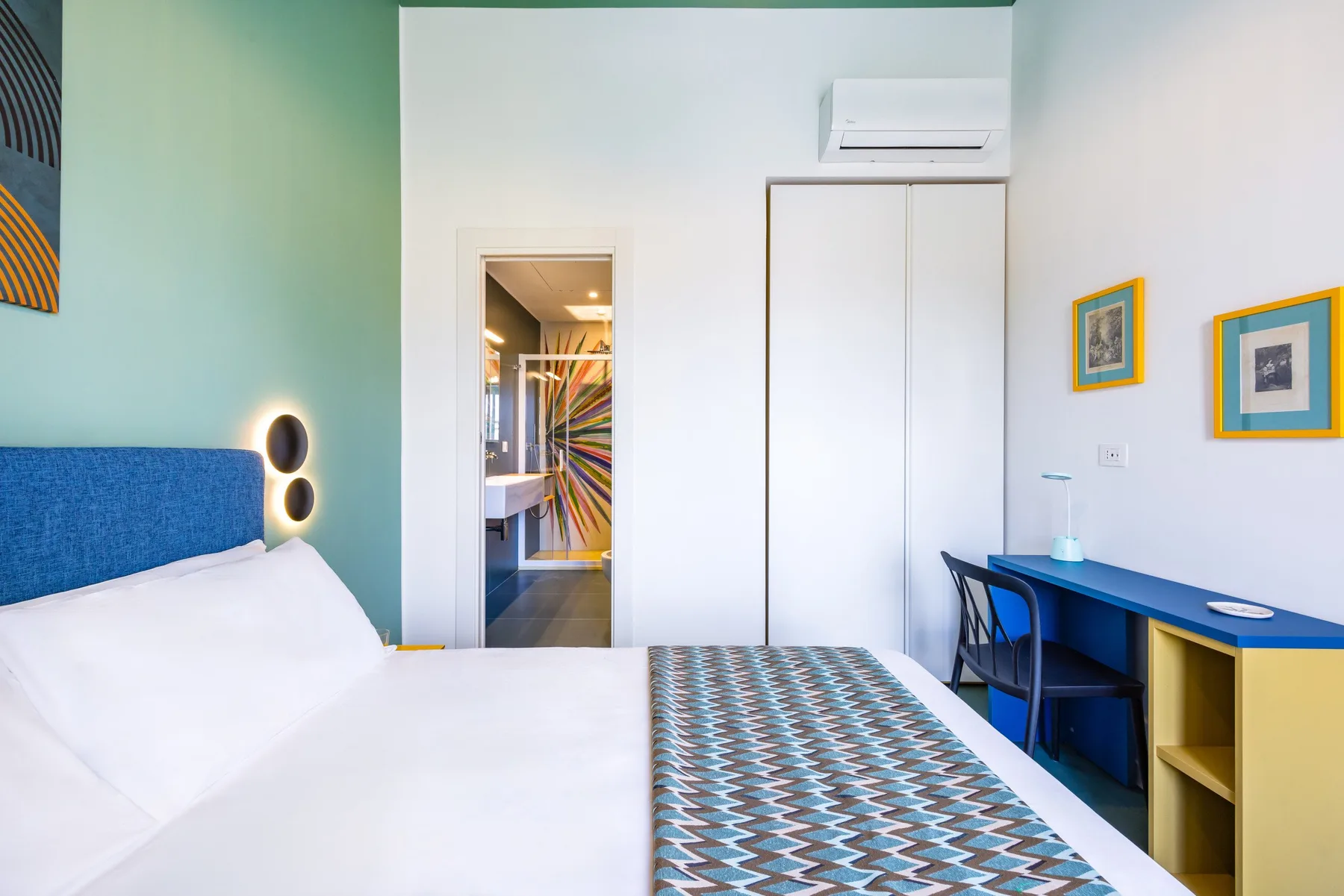 Un dormitorio con una cama, un escritorio azul y aire acondicionado en la pared.