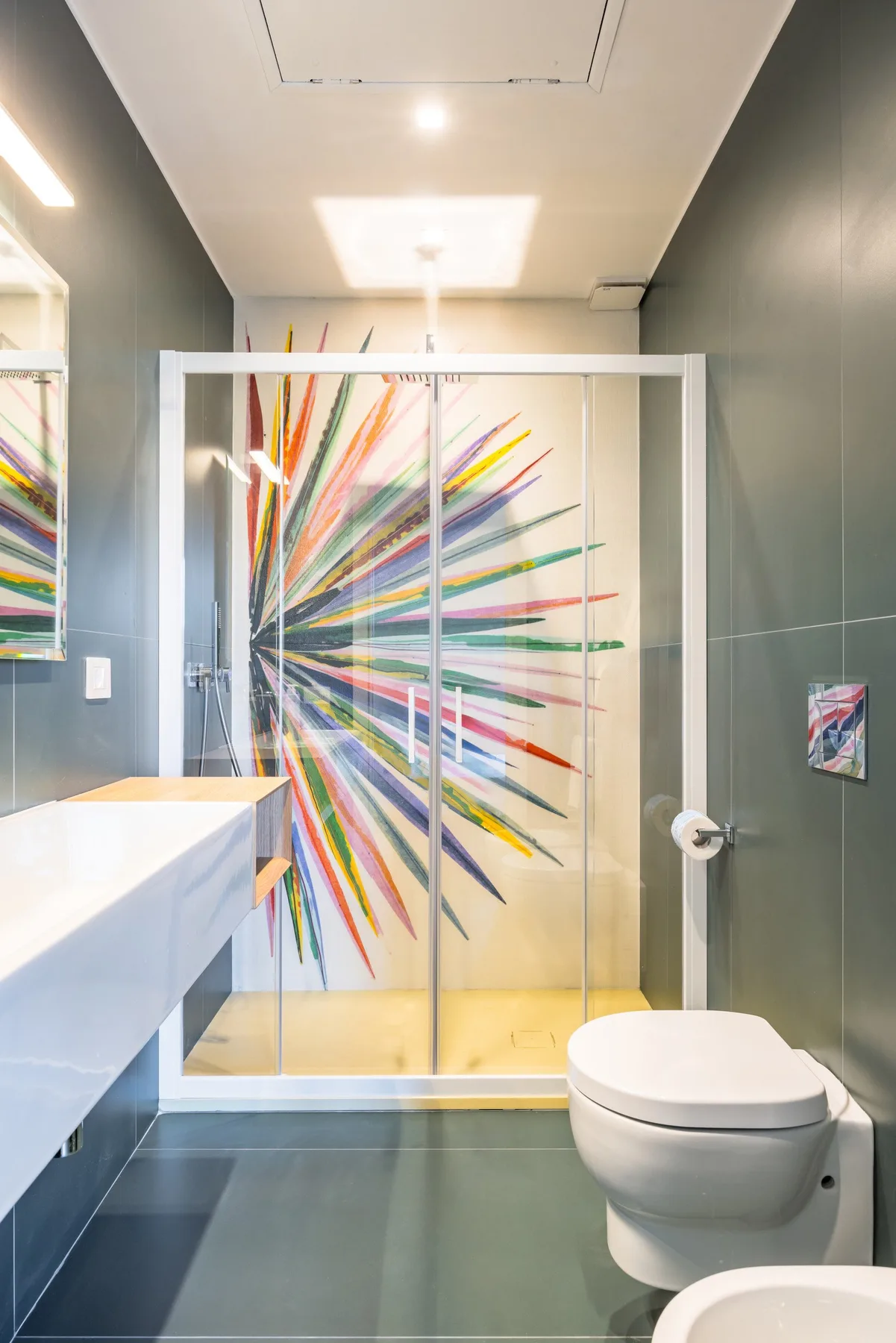 Un baño moderno con ducha de vidrio y arte colorido en la pared.