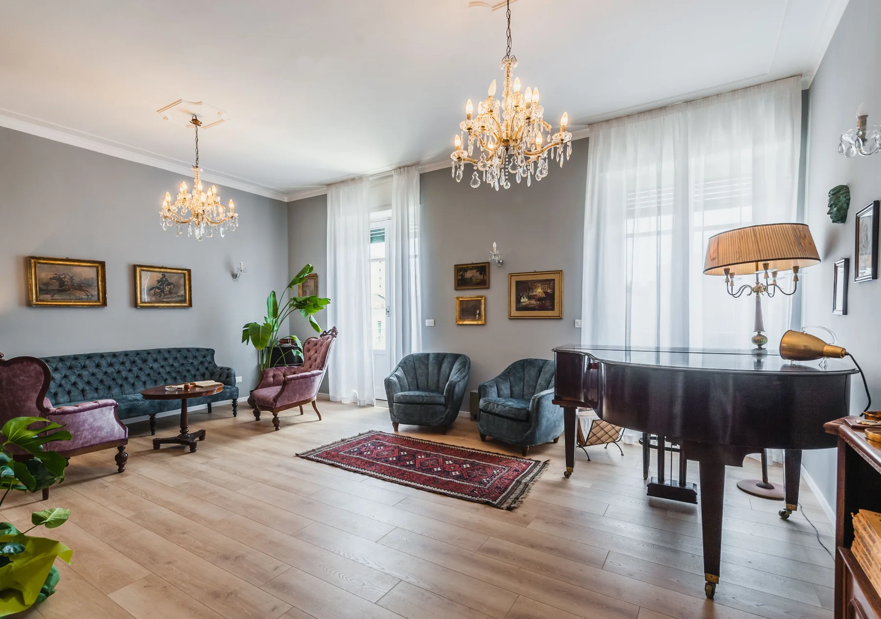 A formal living room with seating, a grand piano, and chandeliers.