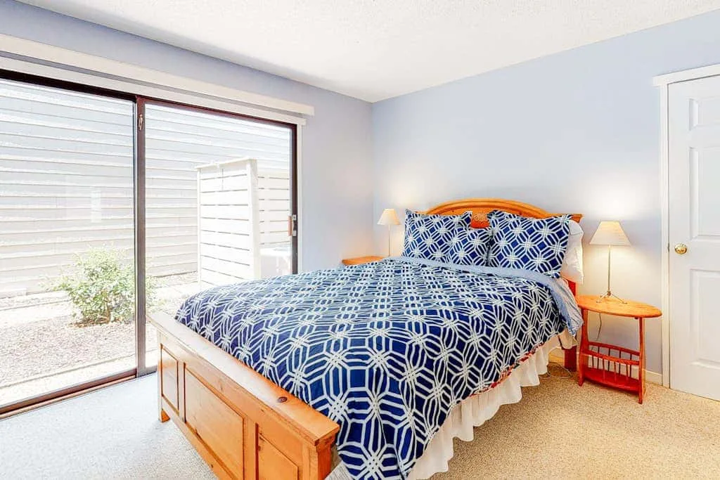 A bedroom with a bed covered in blue patterned bedding beside a sliding glass door.