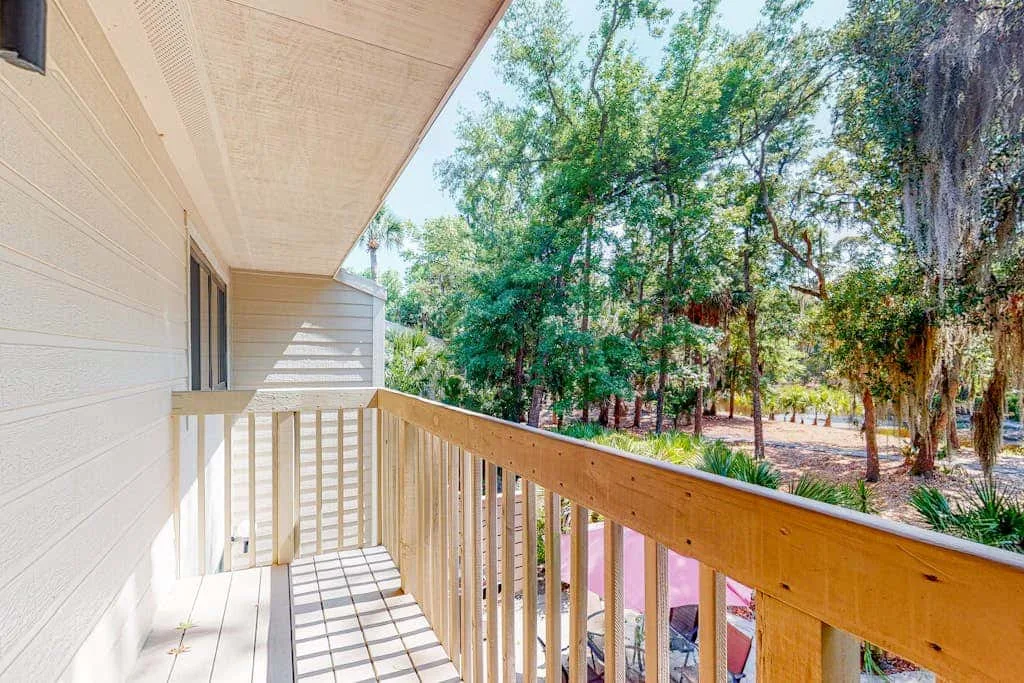 A covered wooden balcony overlooks a wooded outdoor area.