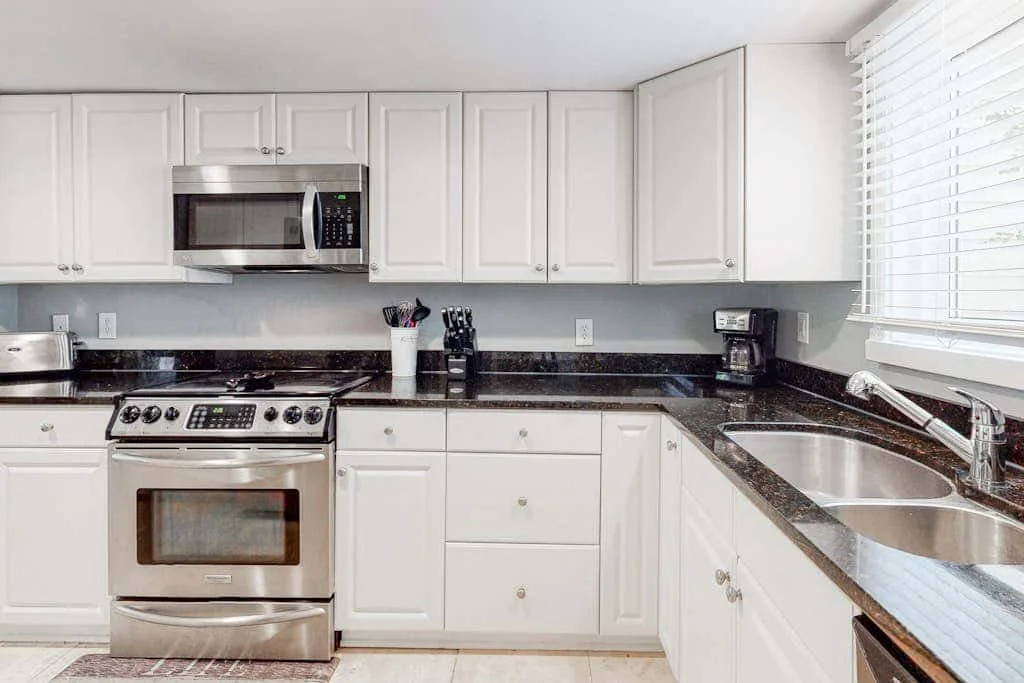 A bright kitchen with white cabinetry, dark countertops, and stainless steel appliances.