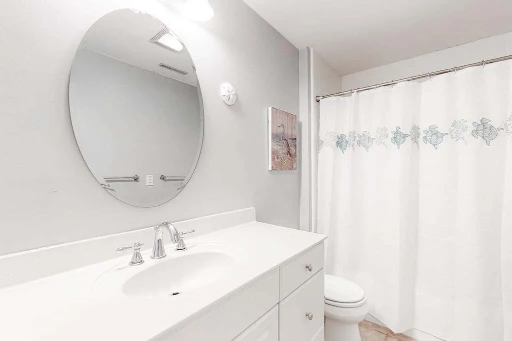 A bright bathroom with a long vanity, oval mirror, and shower curtain.