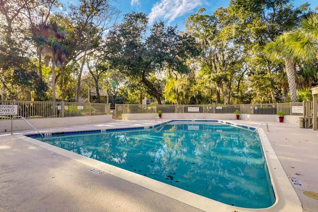 An outdoor swimming pool sits among trees, with a paved deck around it.