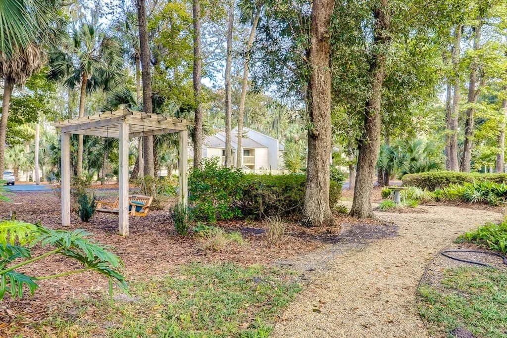 A garden path winds past trees and a wooden pergola with seating.