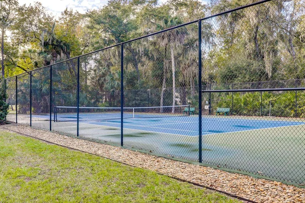 An outdoor tennis court is enclosed by fencing and surrounded by trees.