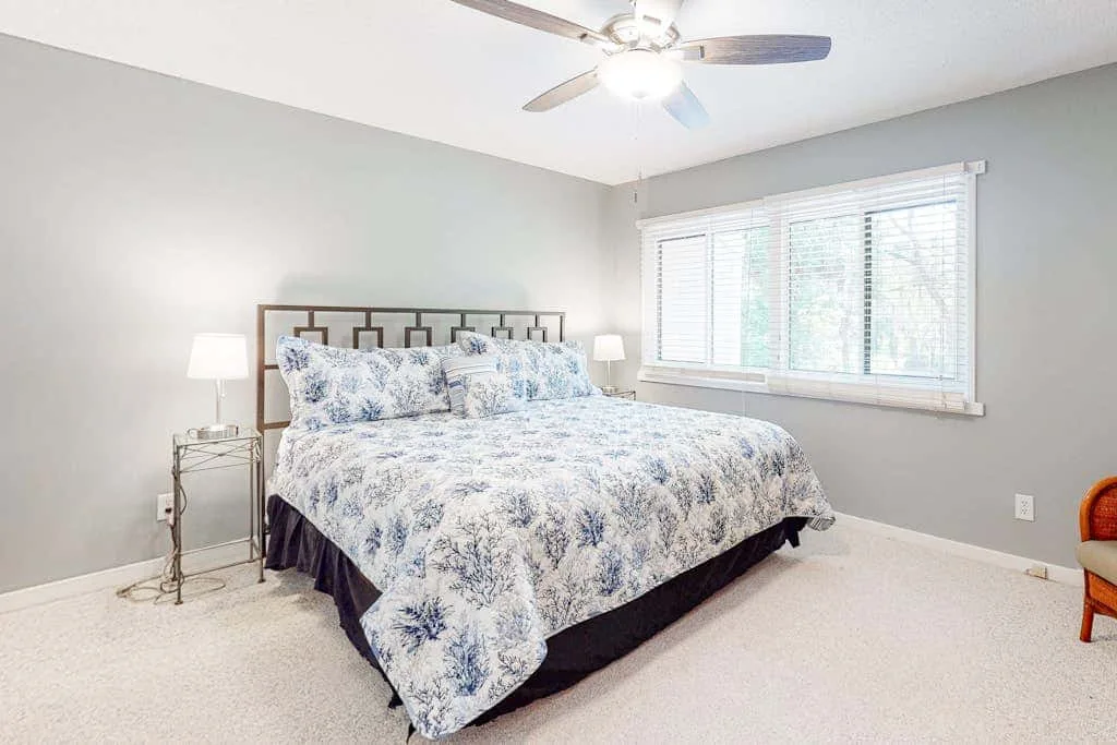 A bedroom with a large bed and a wide window with blinds.