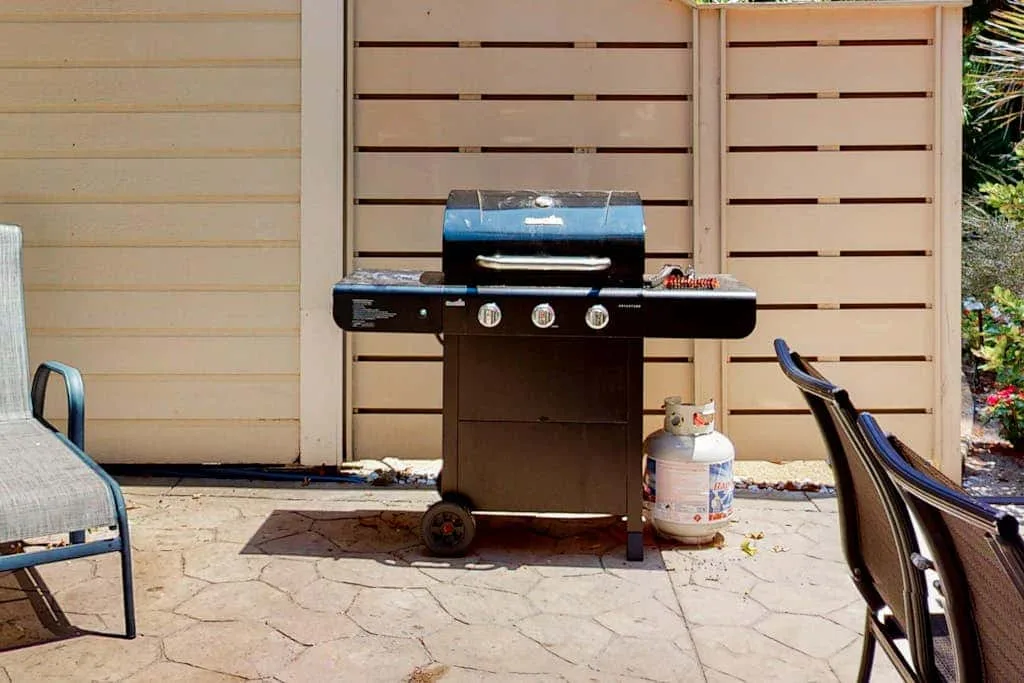 A gas grill stands on a paved patio beside outdoor seating.