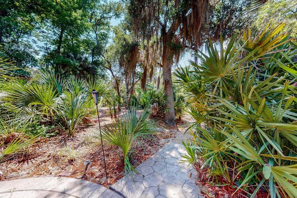 A paved garden path winds through dense greenery and trees.