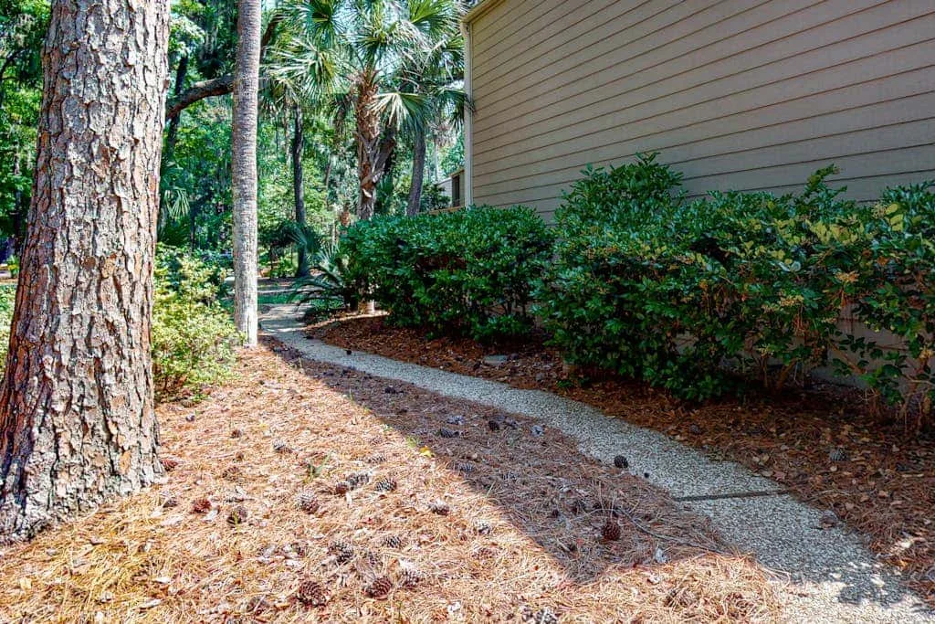 A gravel path curves beside a building through trees and shrubs.