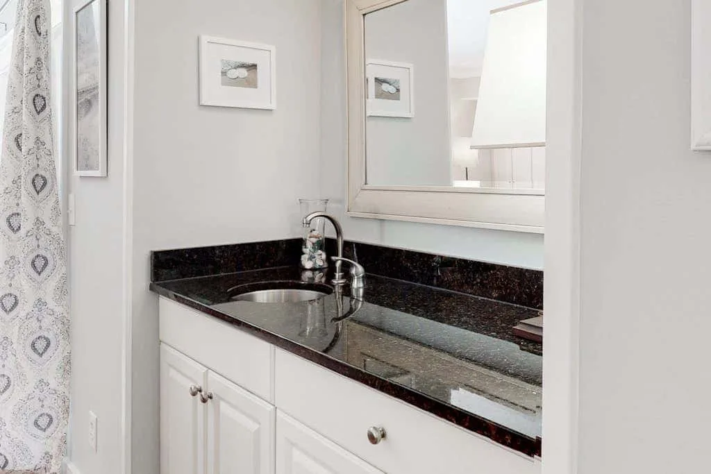 A bathroom vanity with a dark countertop and a patterned shower curtain.