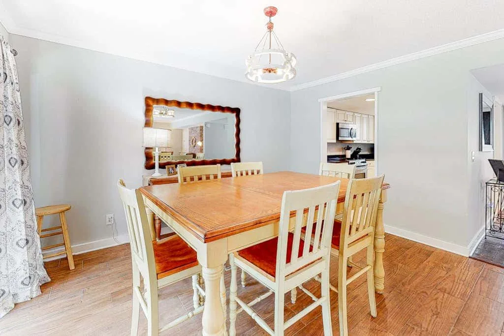 A dining room with a large wooden table and chairs beside an open kitchen.