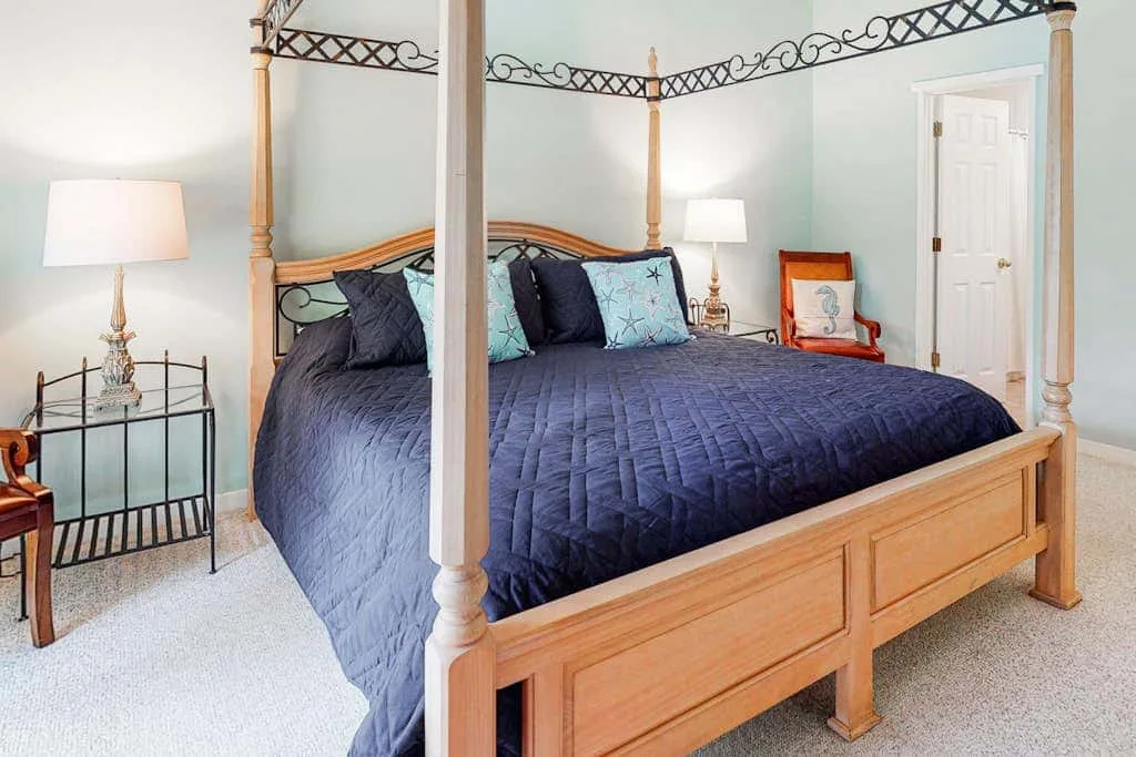 A bedroom with a large wooden bed, dark blue bedding, and bedside lamps.