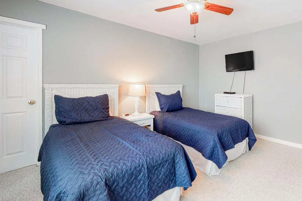A bedroom with two beds covered in blue quilts and a television on the wall.