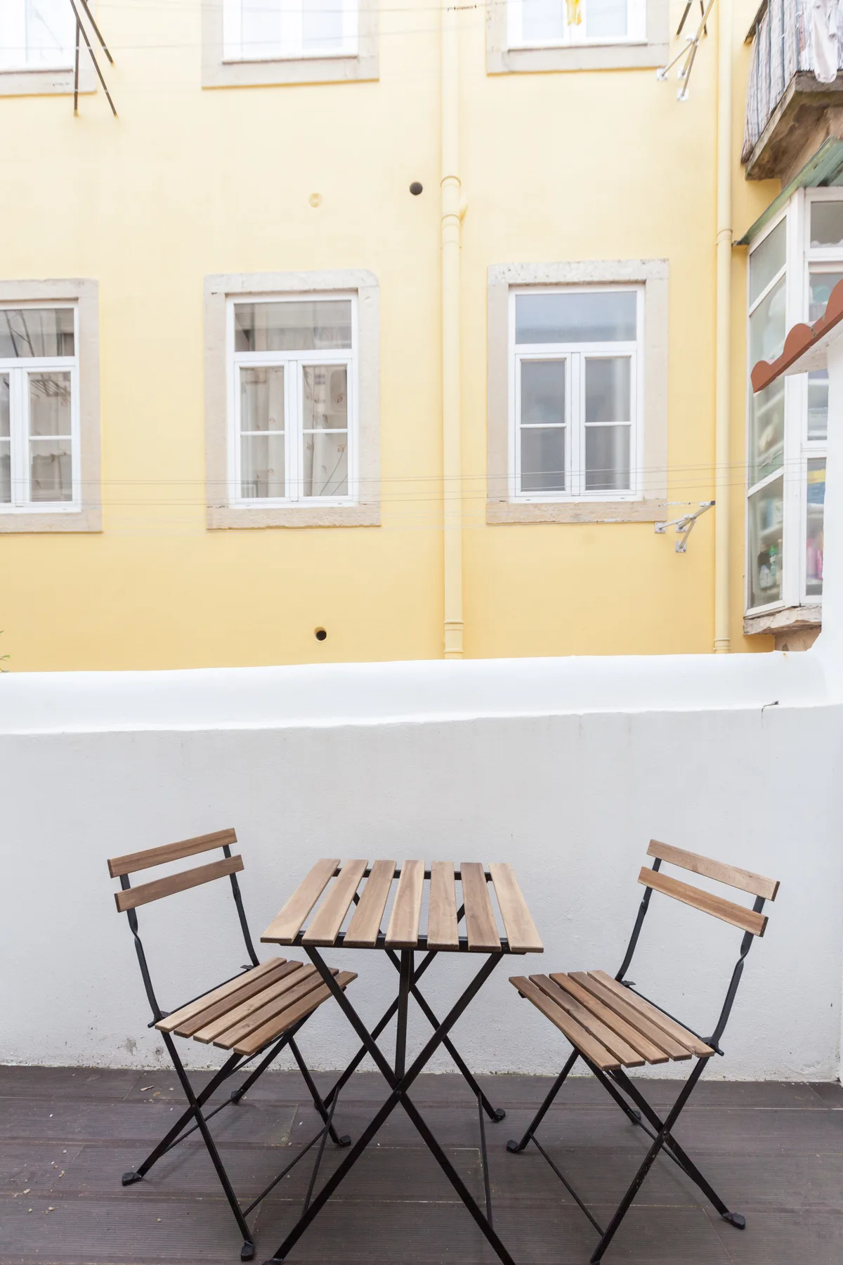 Una pequeña zona de estar al aire libre con mesa y sillas da a un edificio amarillo.